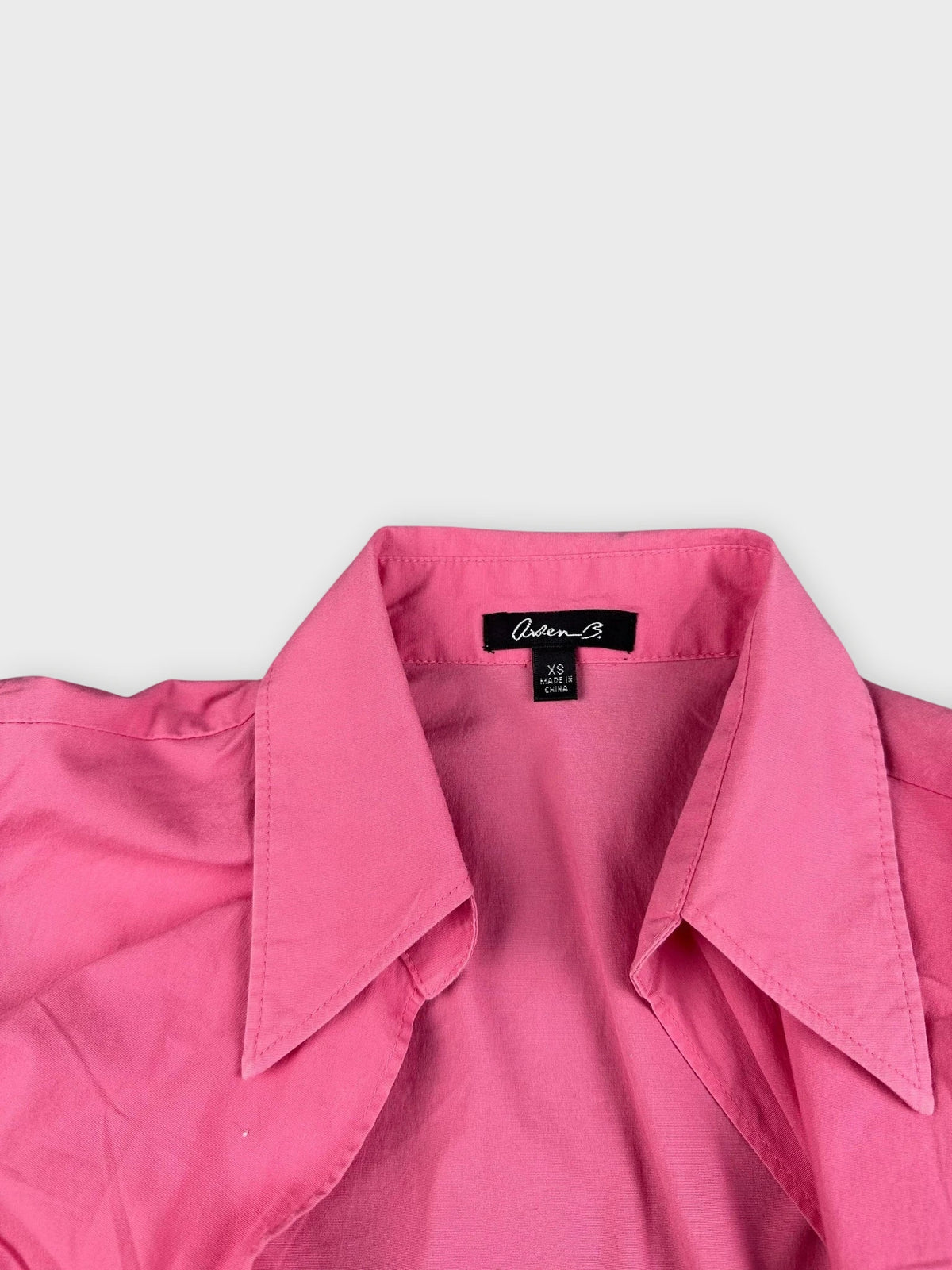 Detail view of a pink sleeveless button-down shirt with large collar.