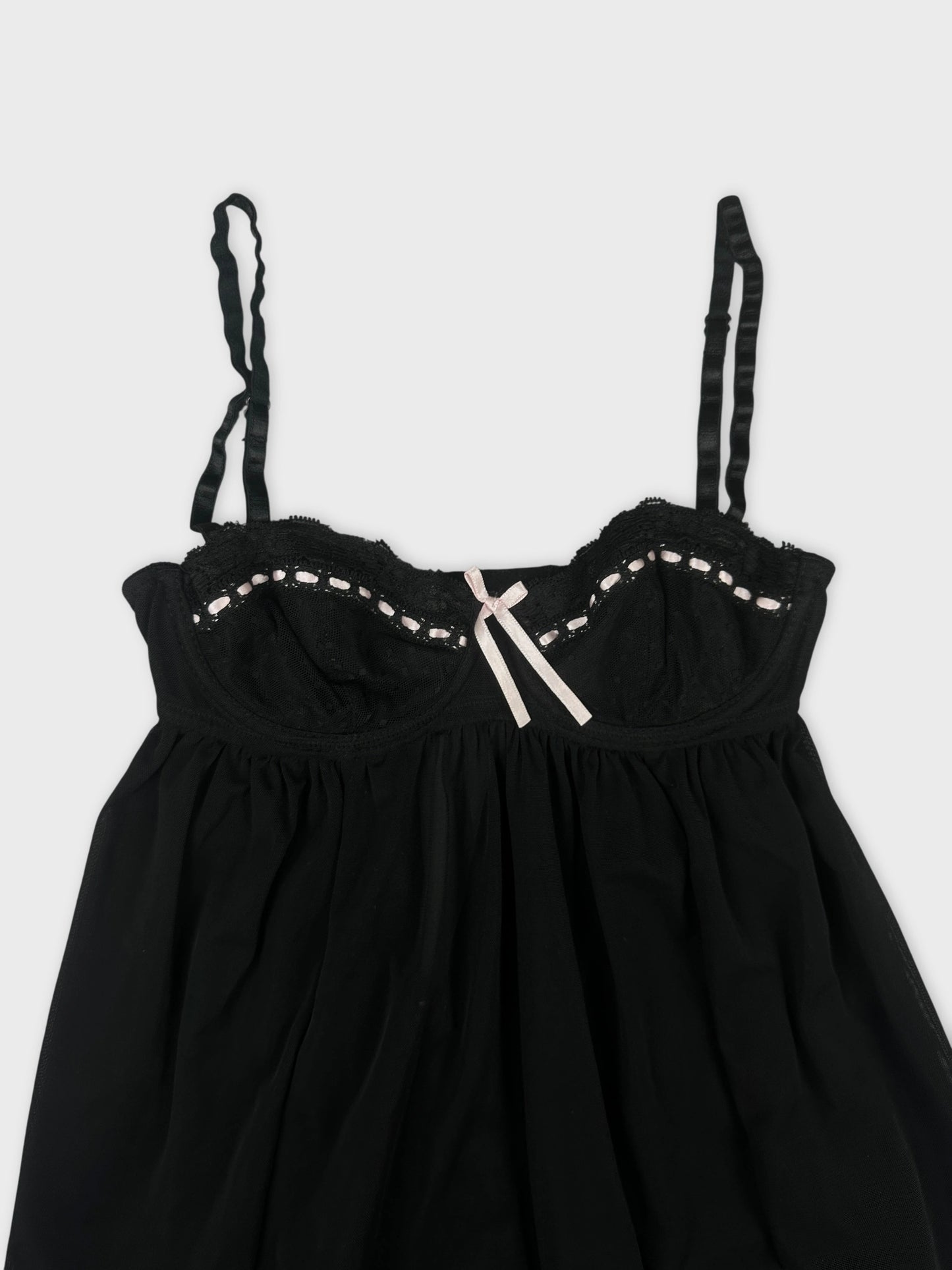 Black lace babydoll top with ruffle hem detail view featuring pink bow accent.