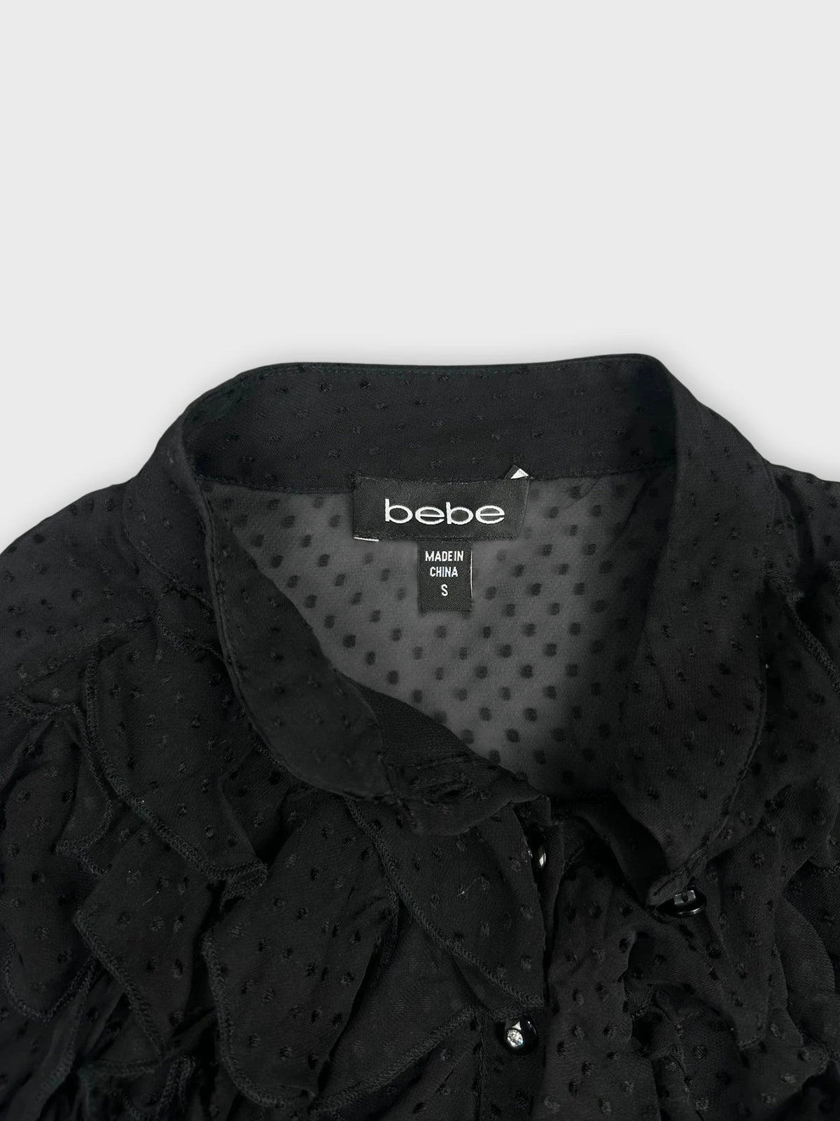 Detail view of a black ruffled blouse featuring button details.