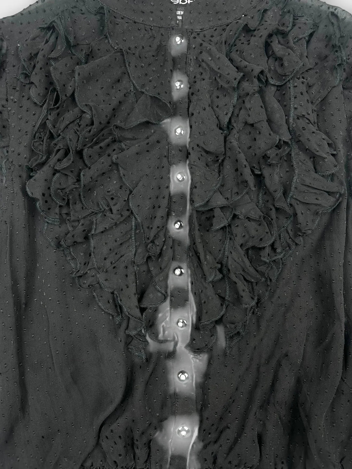 Detail view of a black ruffled blouse featuring shiny button details.