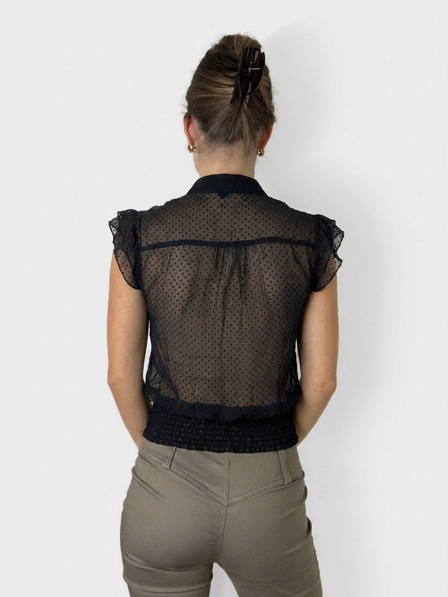Back view of a black ruffled blouse with polka dot pattern and button details.