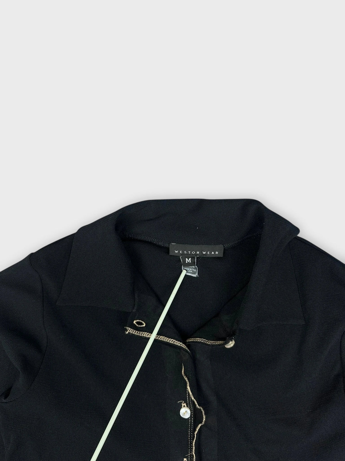 Detail view of a black collared shirt featuring a ruffled hem and pearl buttons.