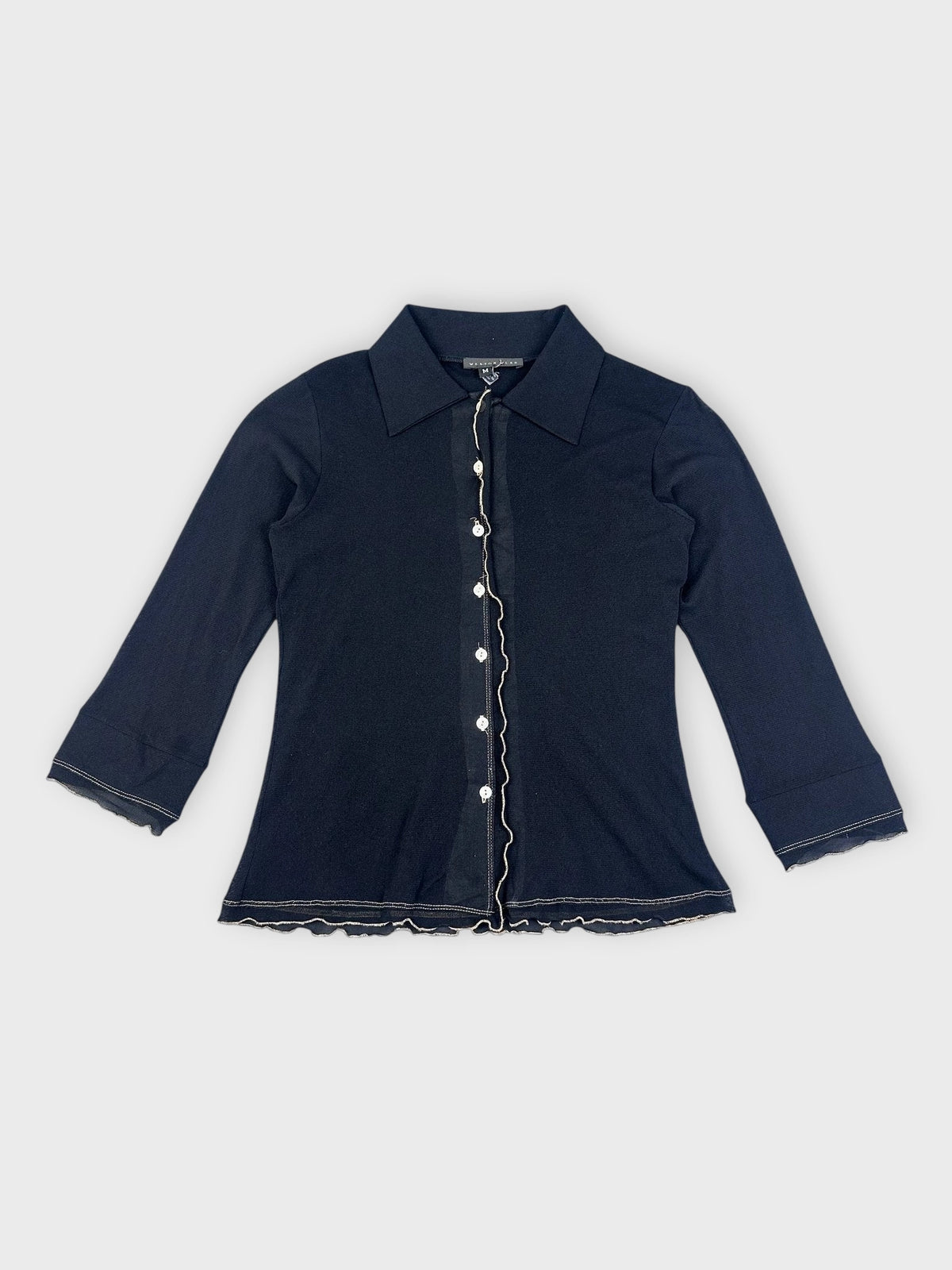 Detail view of chic black collared shirt featuring a ruffled hem.