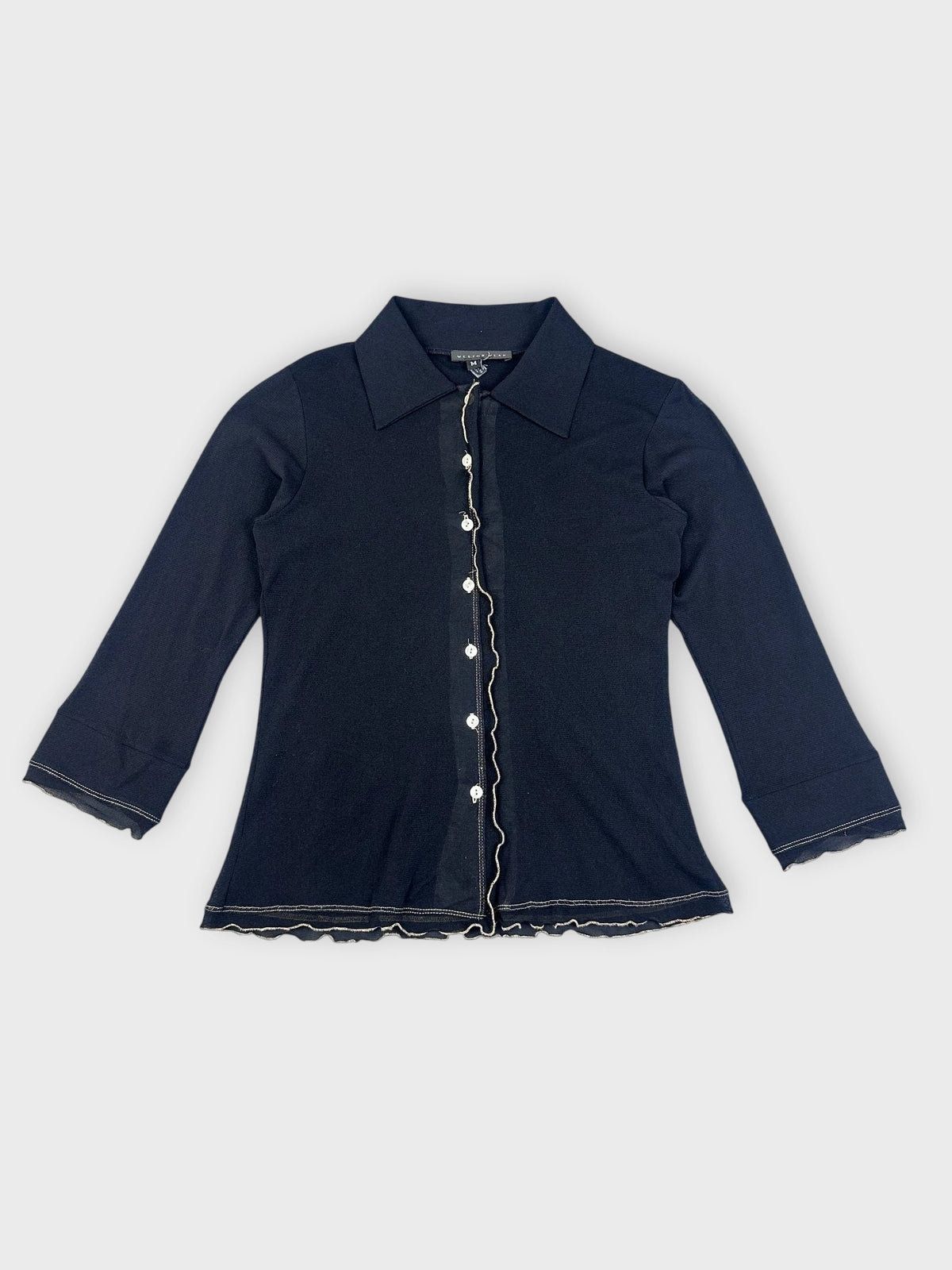Front view of a chic black collared shirt with ruffled hem.