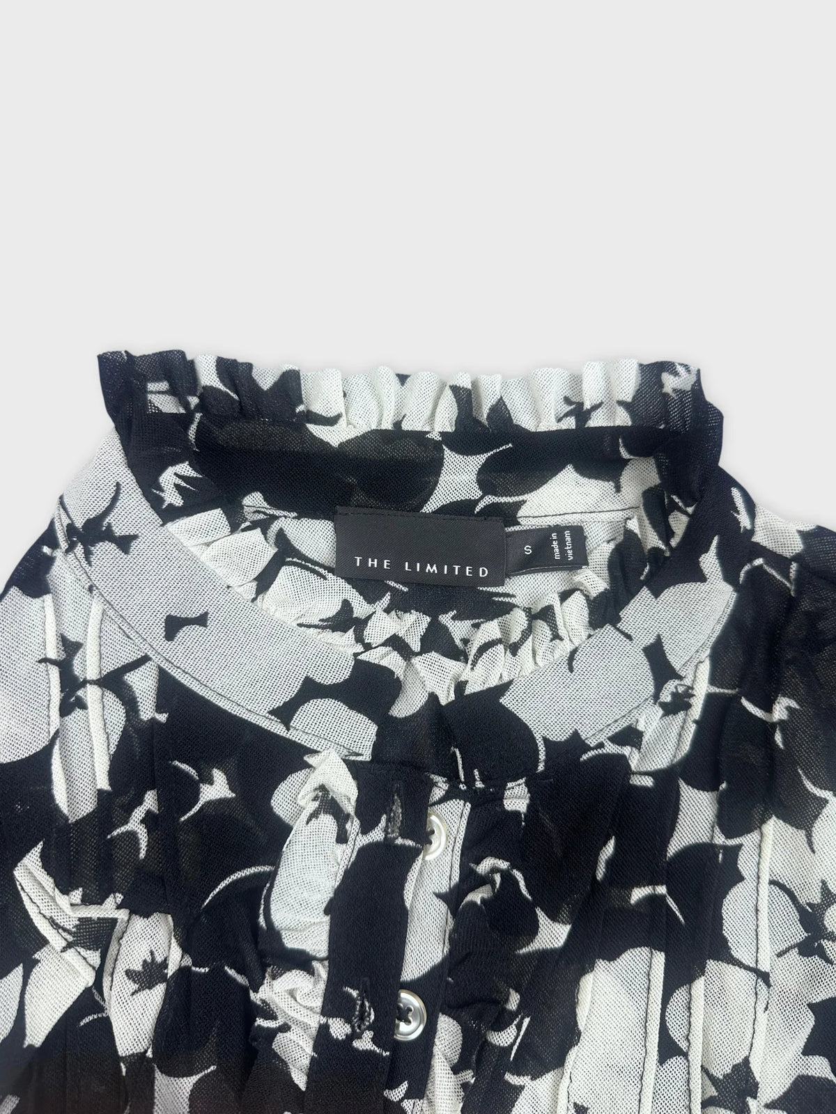 Detail view of black floral playsuit featuring ruffle trim and button closure.