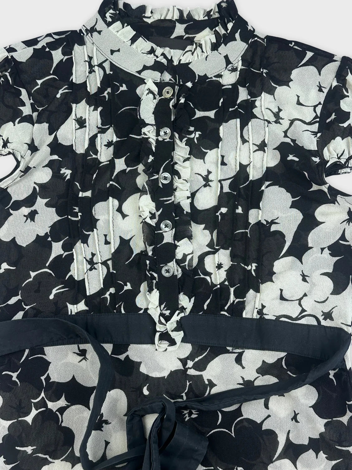 Detail view of a black floral playsuit featuring a ruffle collar and button placket.