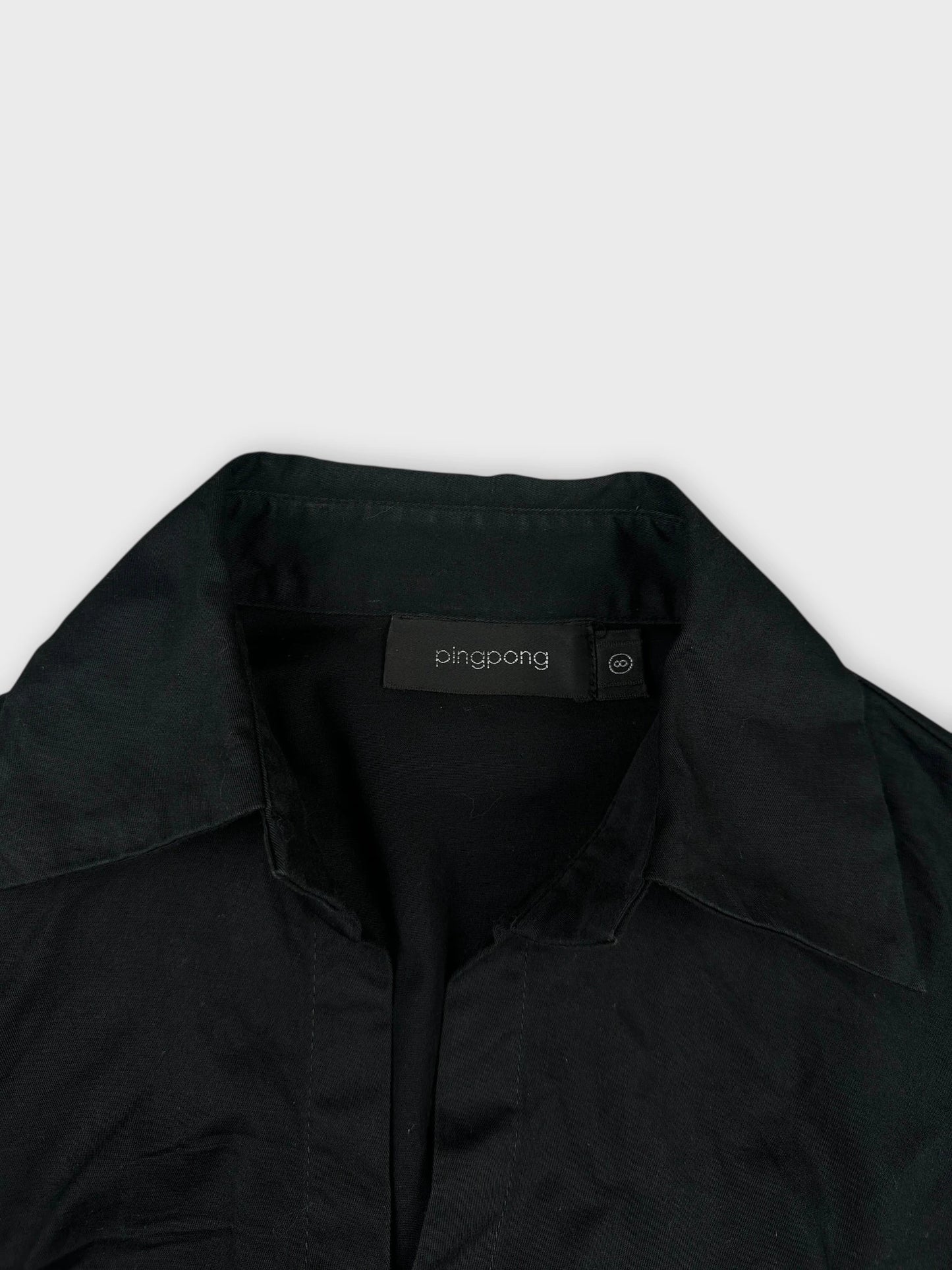 Detail view of a black long sleeve button-up shirt with a V-neck collar.