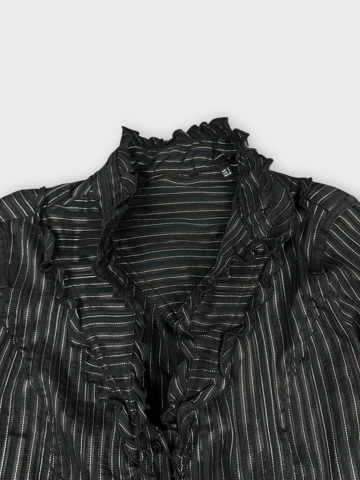 Detail view of a black ruffled blouse with silver stripes.