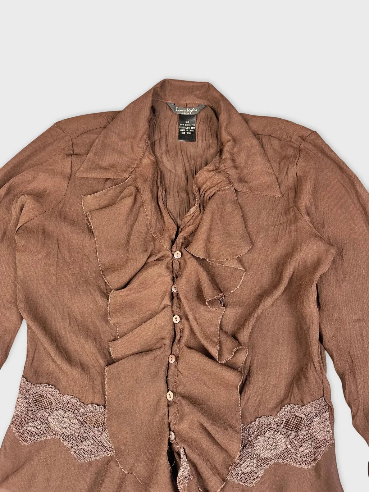 Detail view of brown ruffle blouse featuring lace trim and button closure.