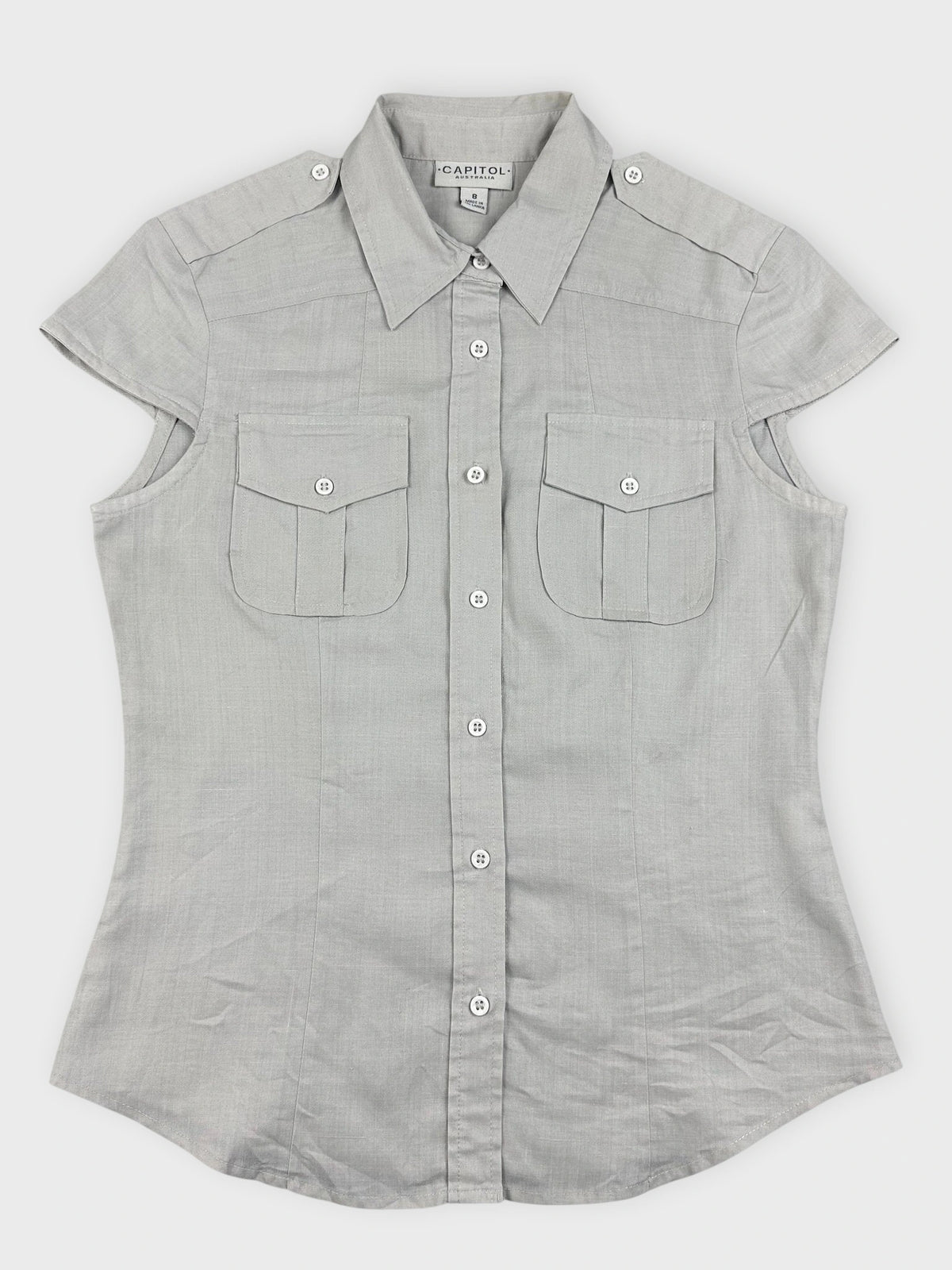 Detail view of light beige button-up top with button closure and pocket features.