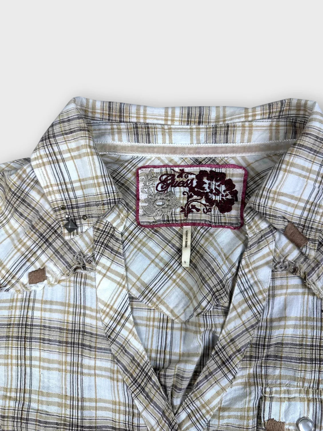 Detail view of a plaid button-up shirt in beige and yellow with frayed hem.