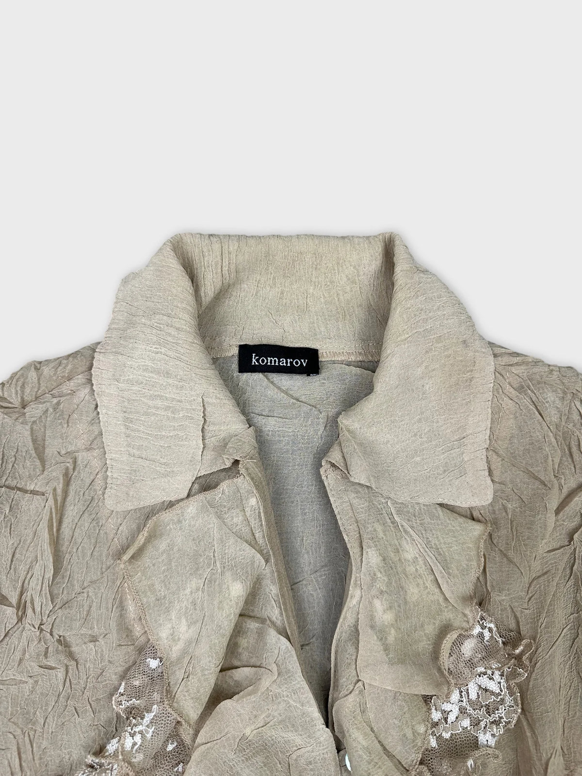 Detail view of a beige ruffled long sleeve top with lace trim.