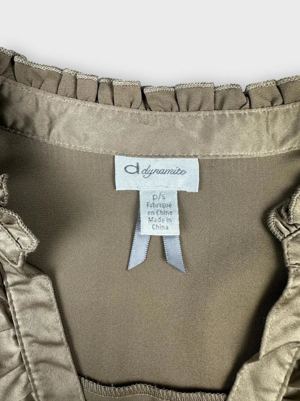 Detail view of taupe satin blouse with ruffled neckline trim.
