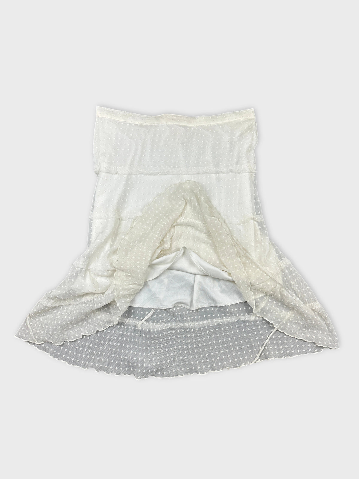 Detail view of a cream sheer mini skirt with polka dots and ruffled hem.