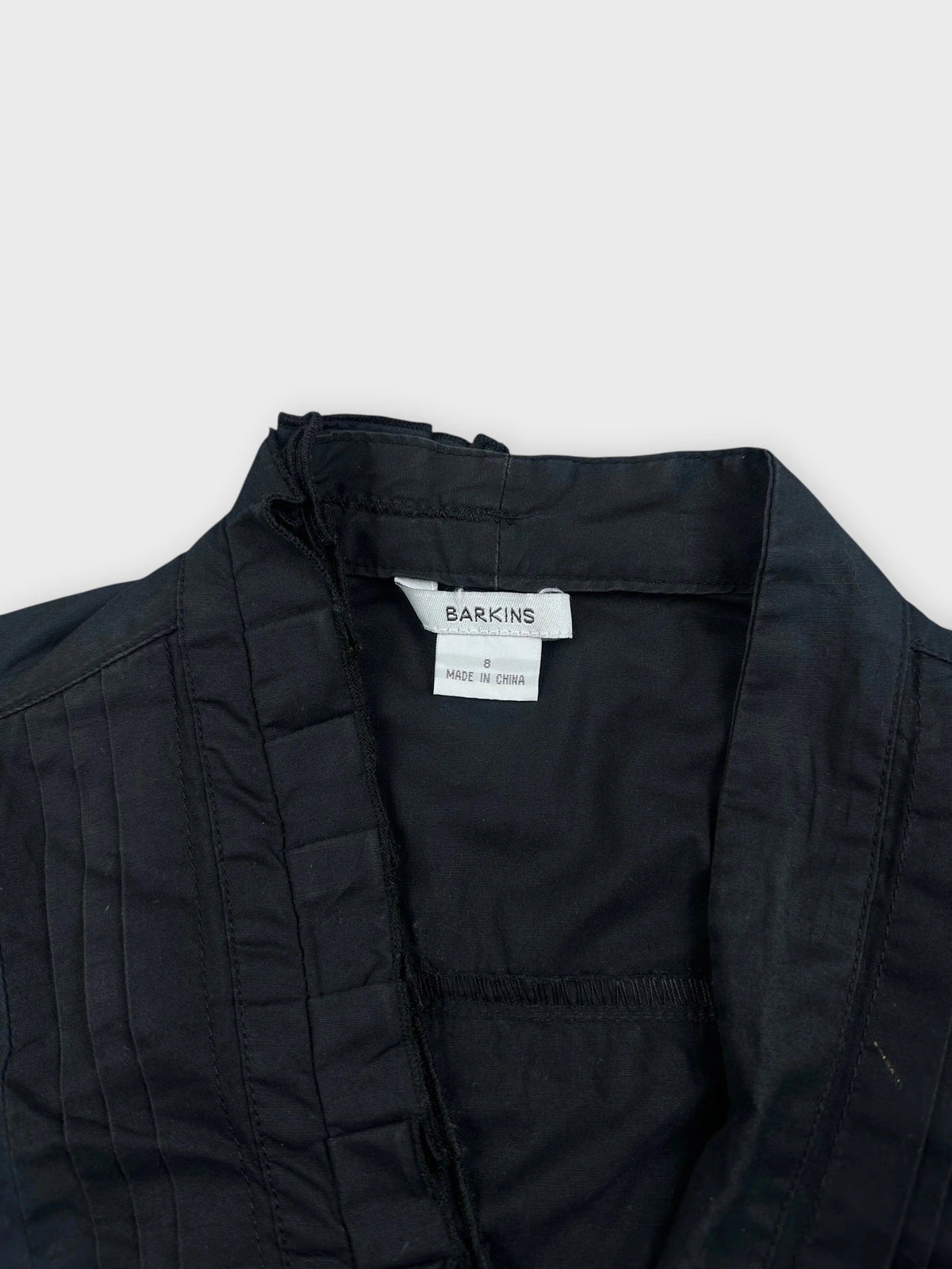 Detail view of a black sleeveless ruffled top showing fine pleats and structured front.