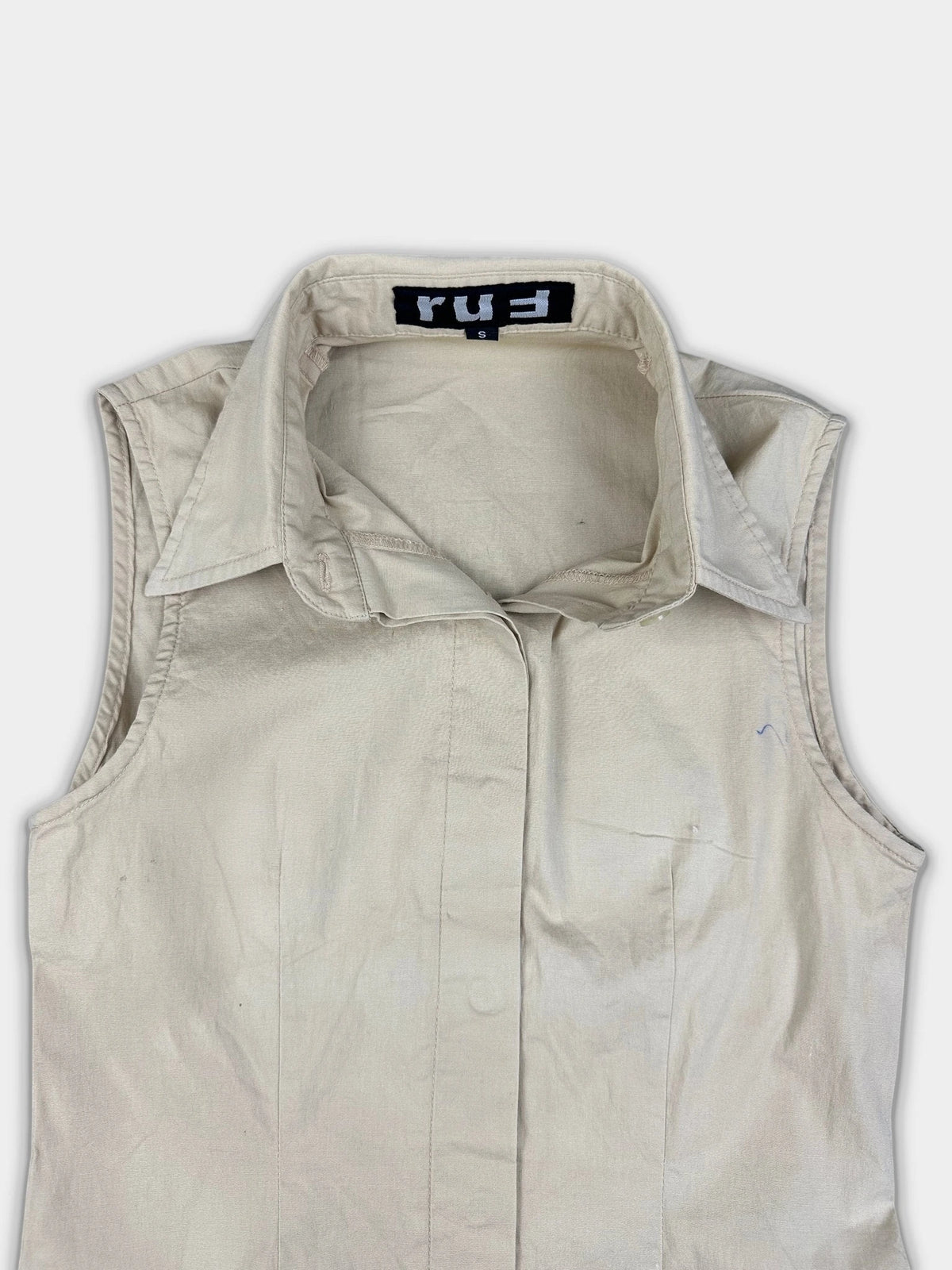 Detail view of a sleeveless off-white top featuring a sharp collar.