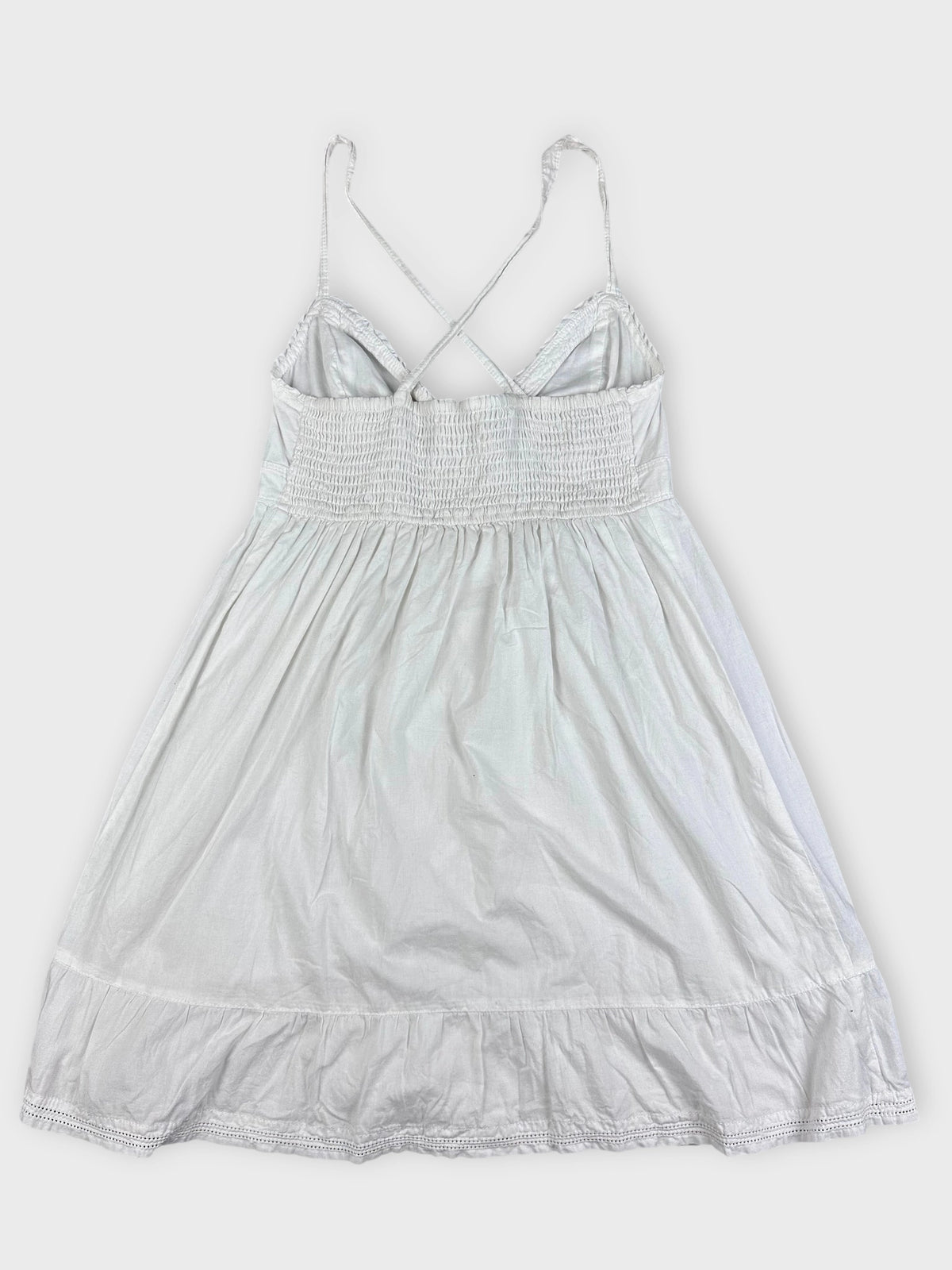 Back view of a white cotton strap dress with smocked bodice and ruffled hem.