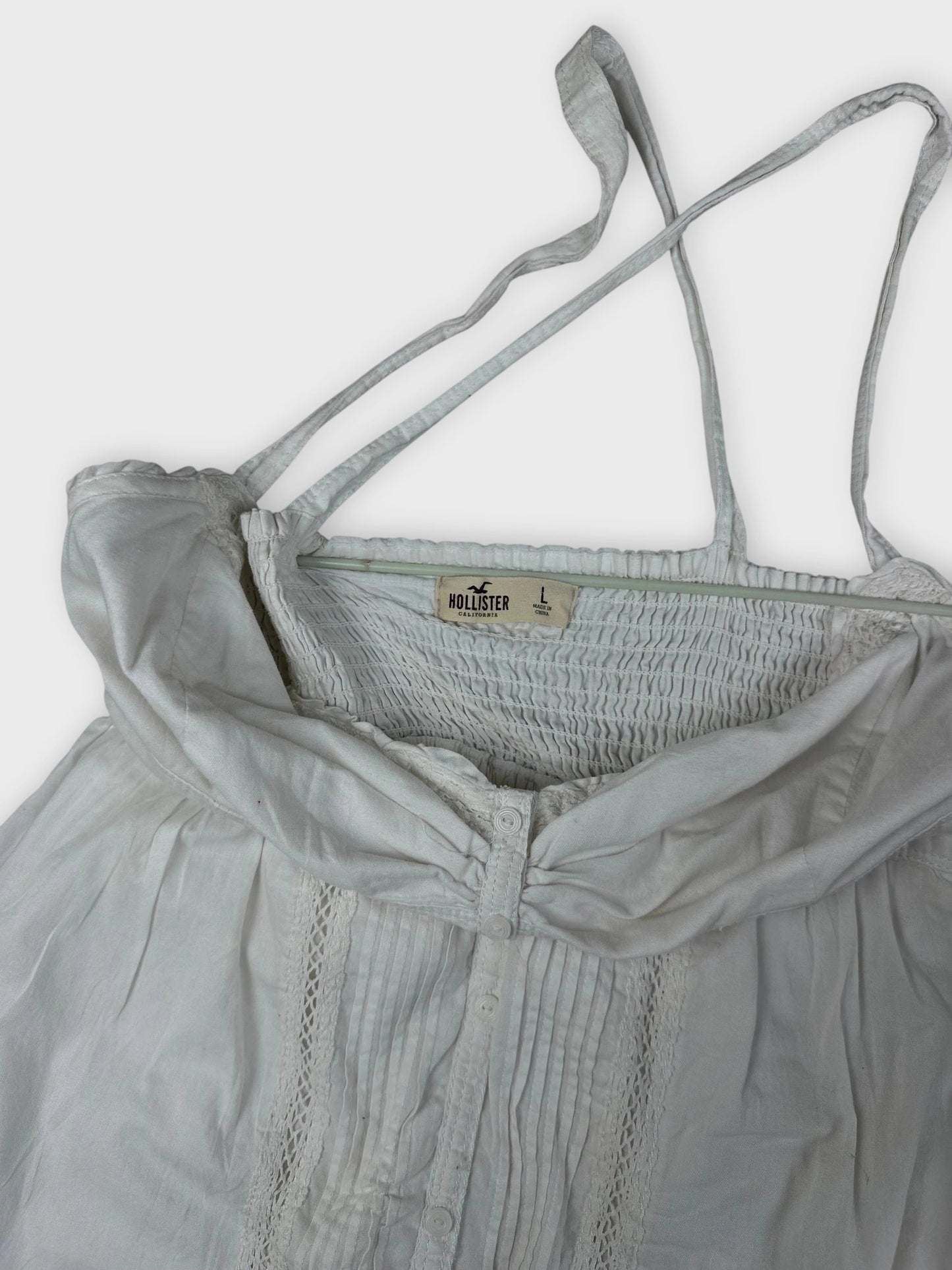 Detail view of white cotton strap dress featuring button and lace detailing.