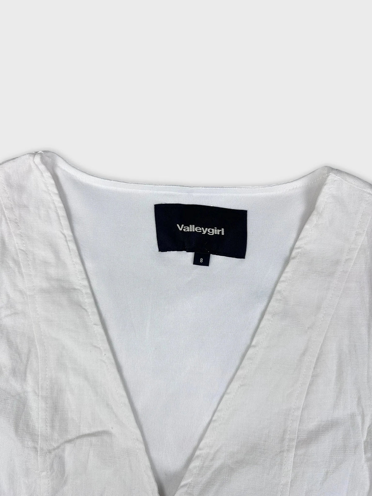 Chic white linen top detail view with V-neckline and lace-up sides.