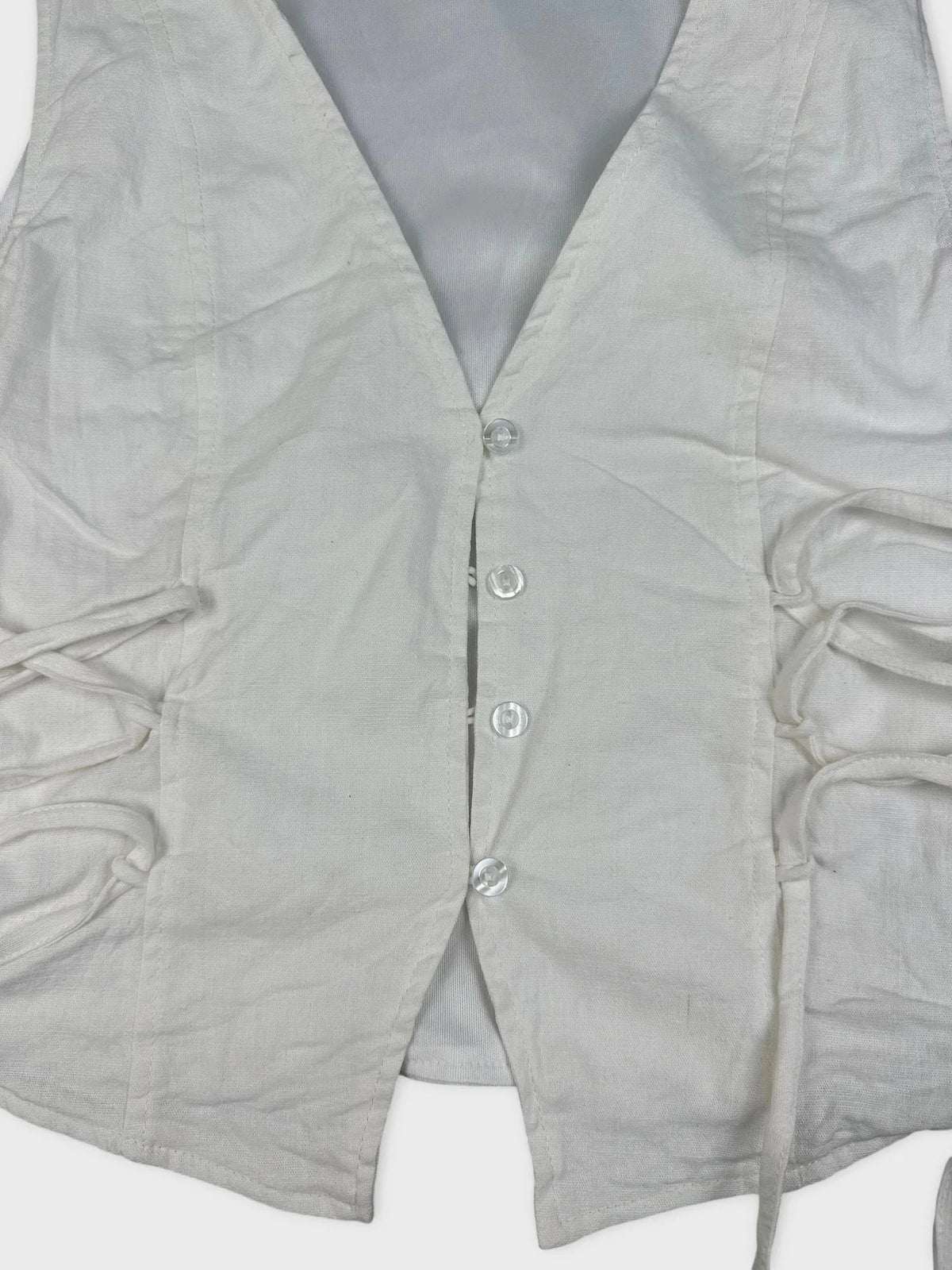 Detail view of a white lace-up linen top with side gathers.
