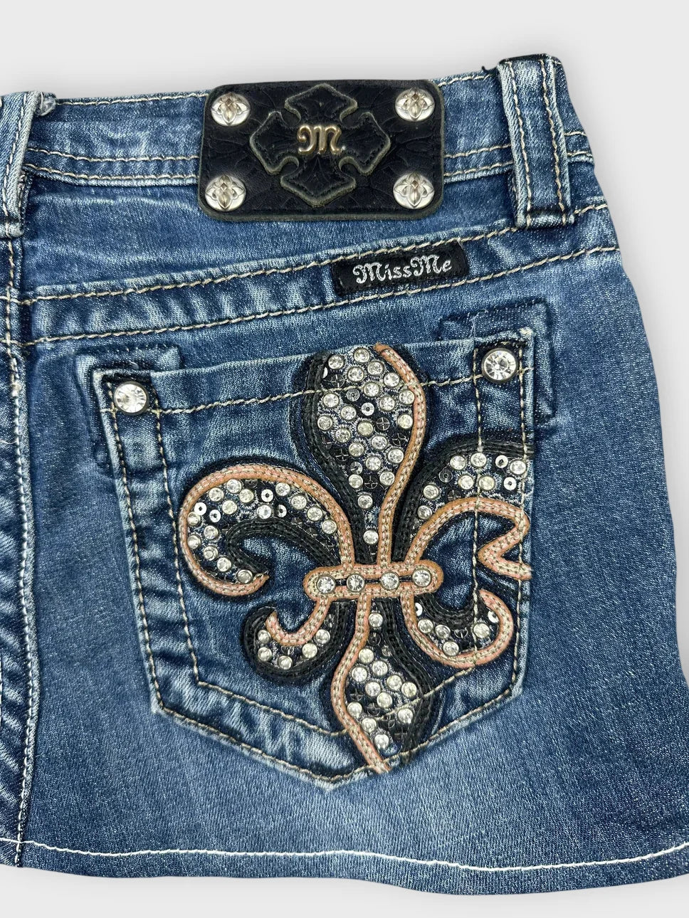 Detail view of a blue denim skirt featuring a decorated back pocket.