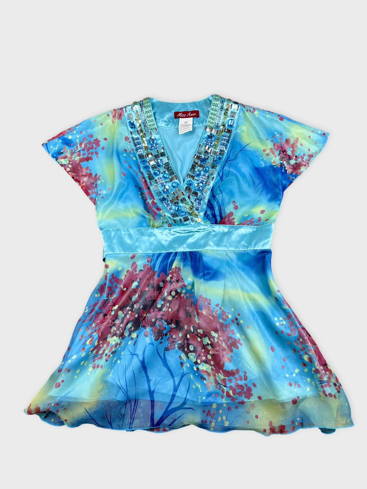 Detail view of a colorful blue top with floral print and embellished neckline.