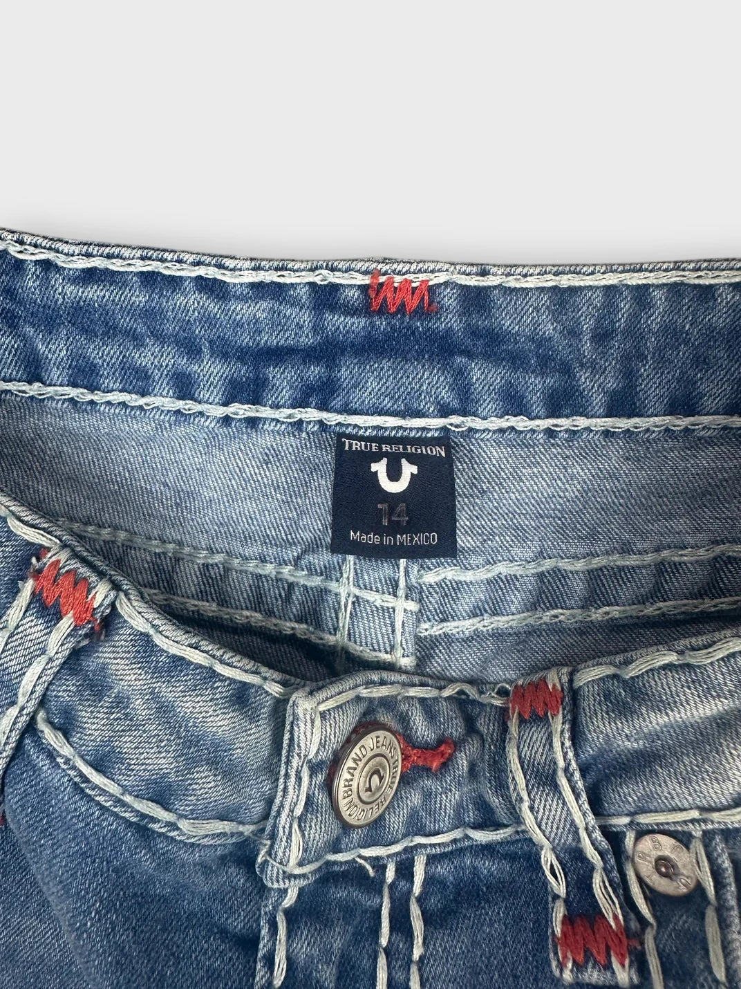 Detail view of denim shorts in blue featuring edgy red stitching.