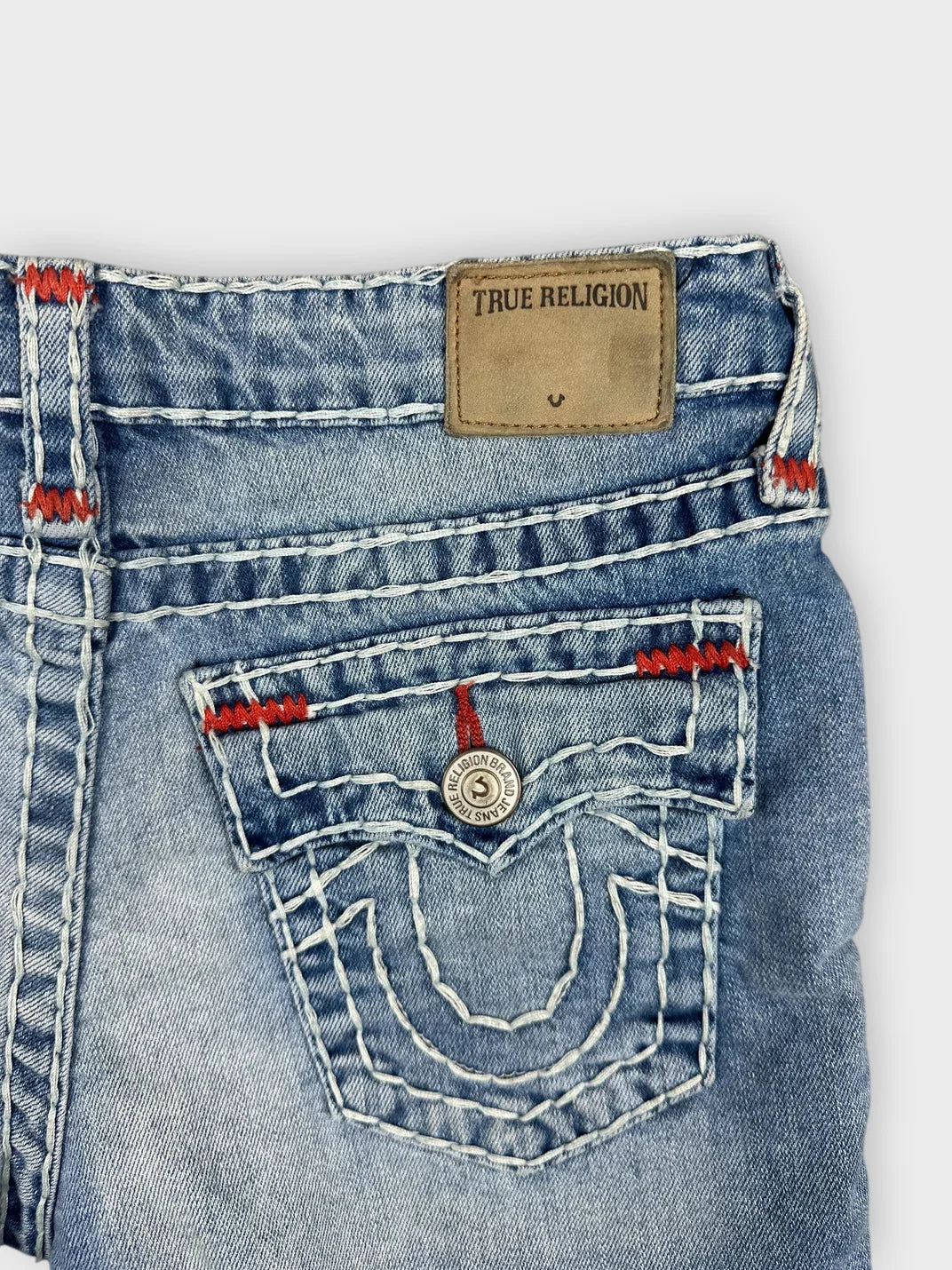 Detail view of blue denim shorts featuring red stitching and back pocket design.