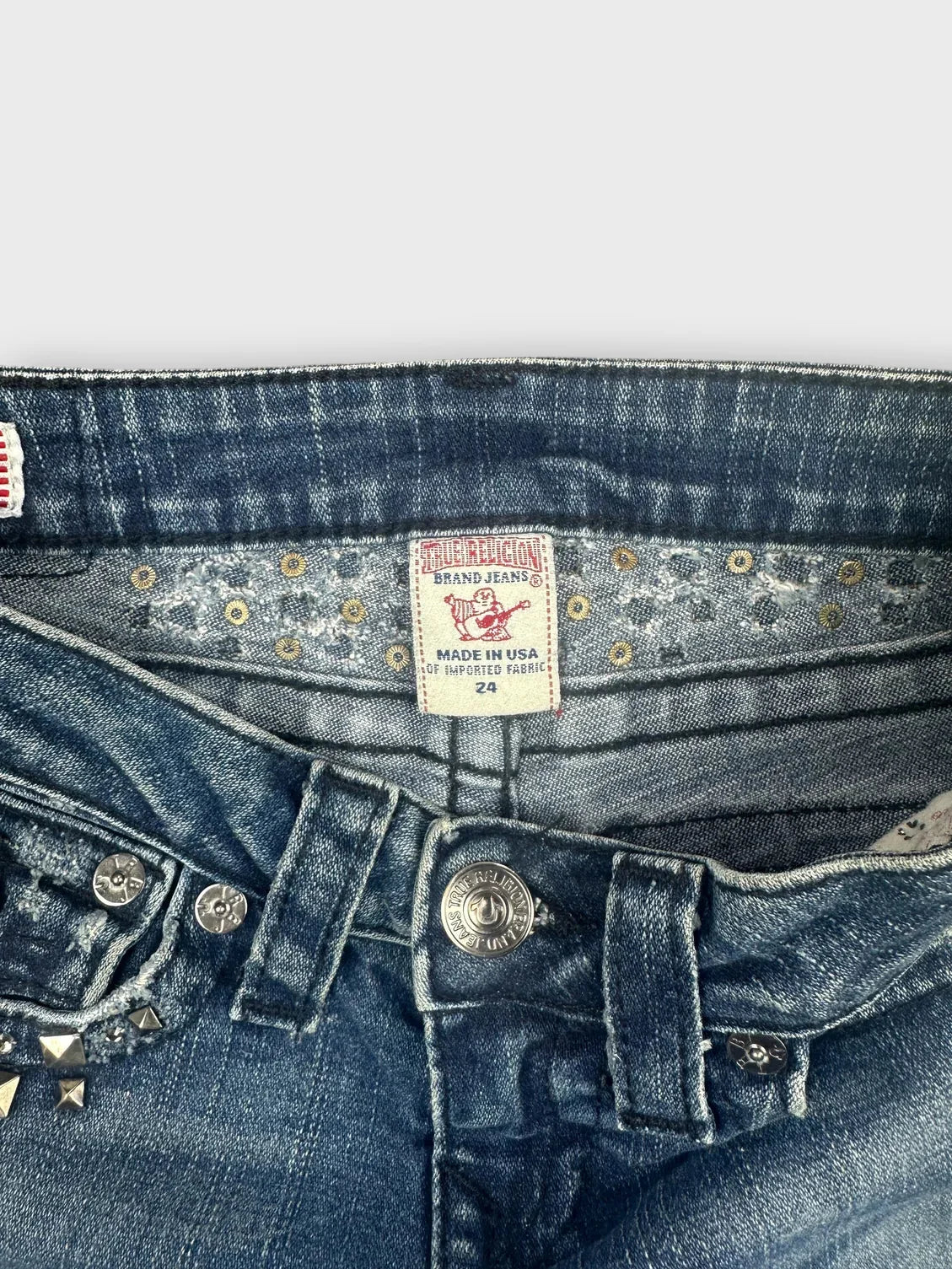 Detail view of denim shorts in blue with studded details and a button closure.