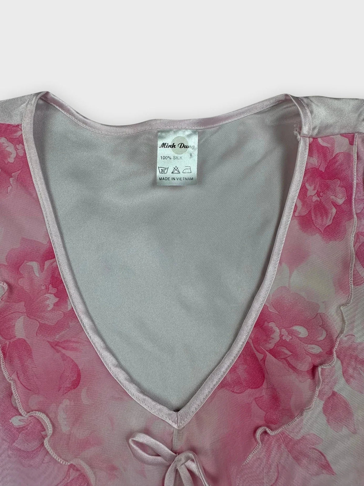 Detail view of a floral pink silk sleeveless top with a V-neck and ribbon tie.