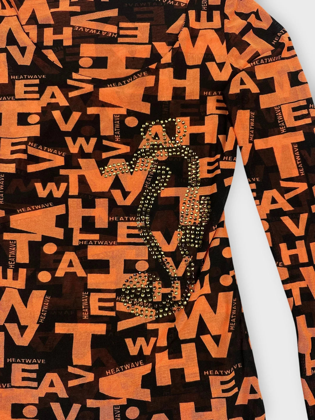 Detail view of bold orange long sleeve top with black print and rhinestone design.