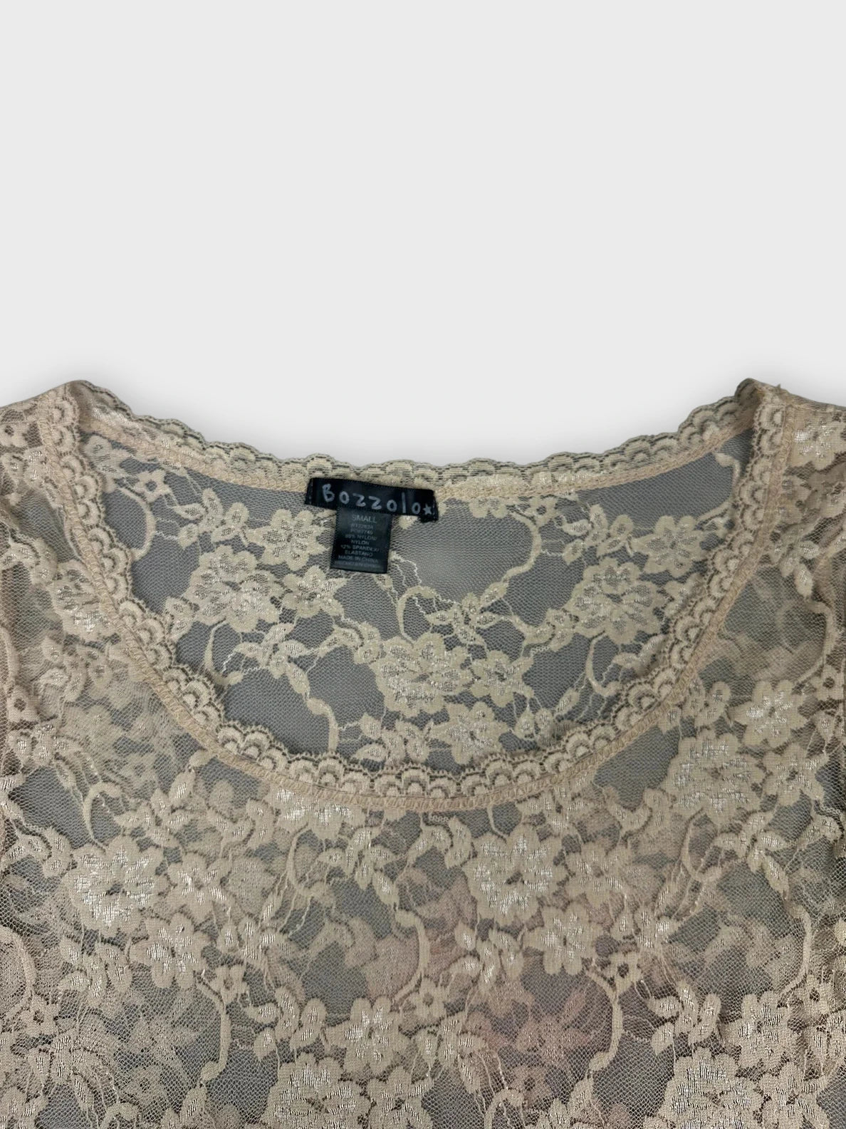Detail view of a lace long sleeve beige top with floral pattern.