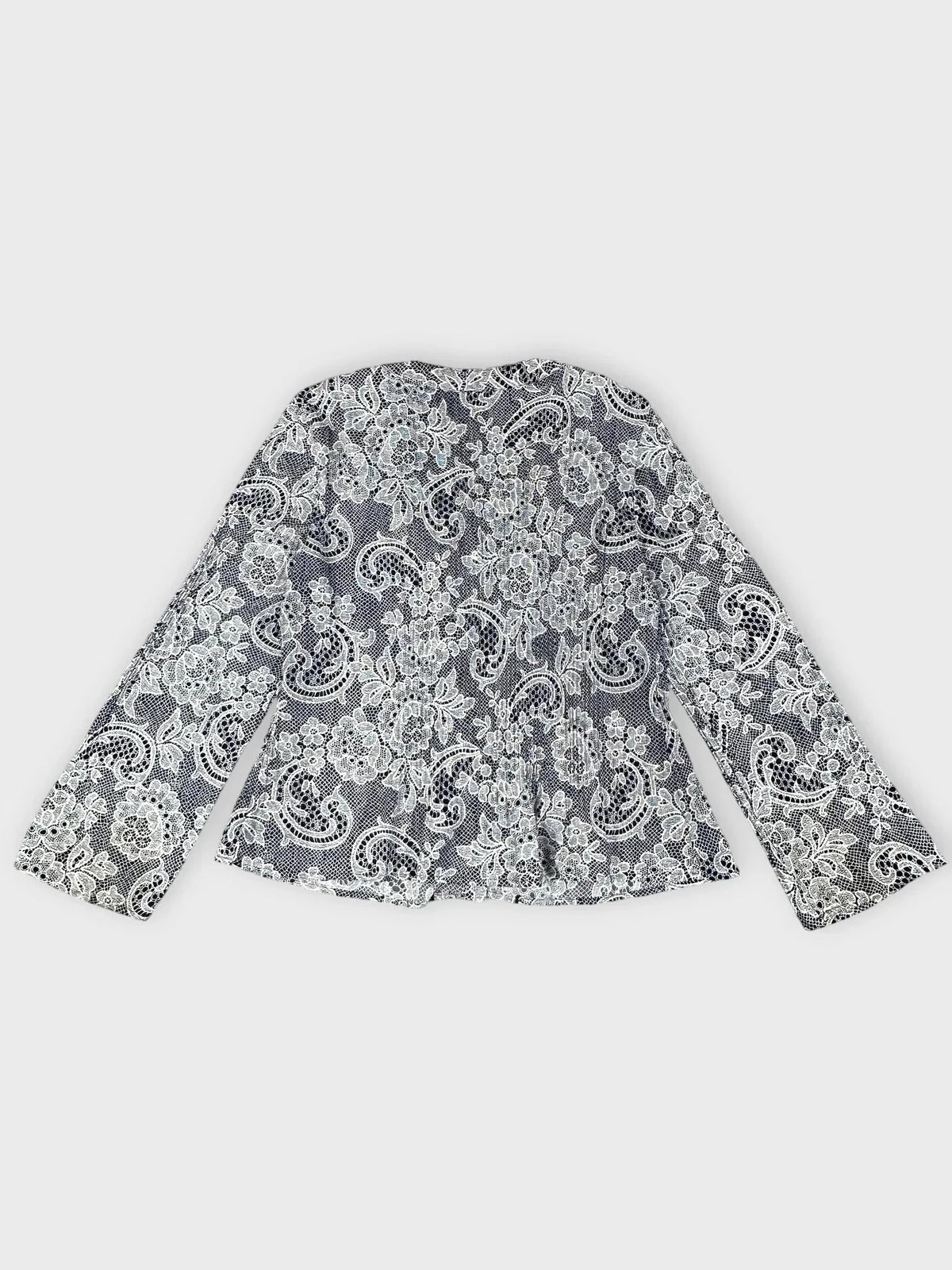 Back view of a lace-print button-up blouse in black and white with ruffle trim.