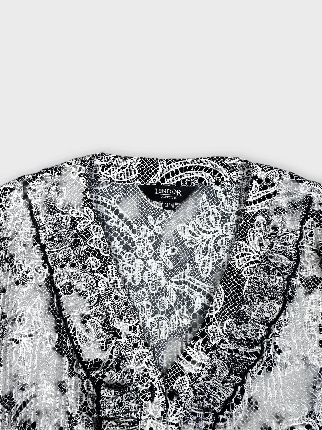 Detail view of black and white lace-print button-up blouse with ruffle trim.