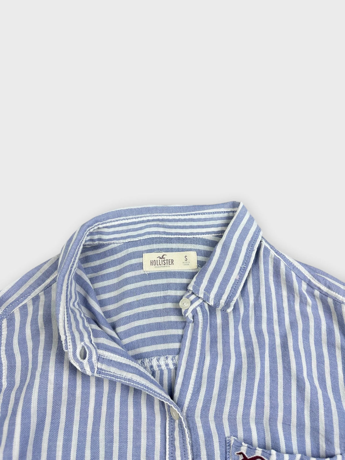 Detail view of a blue and white striped button-up shirt with a collar.