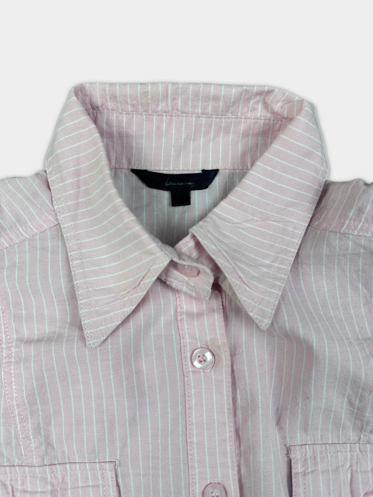 Detail view of a pink pinstripe short sleeve shirt with collar and buttons.