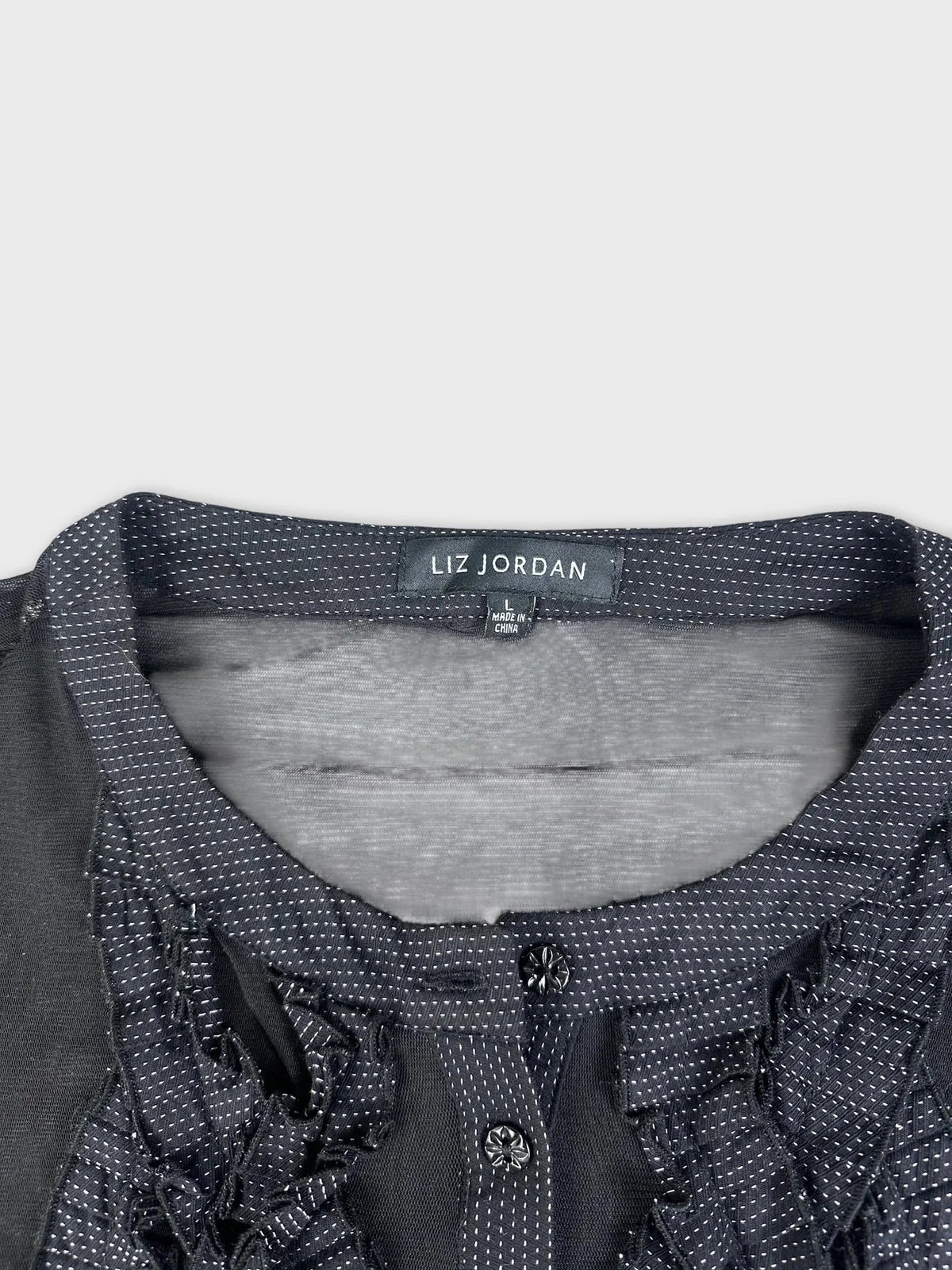 Detail view of sheer black button-up top with ruffle detail.