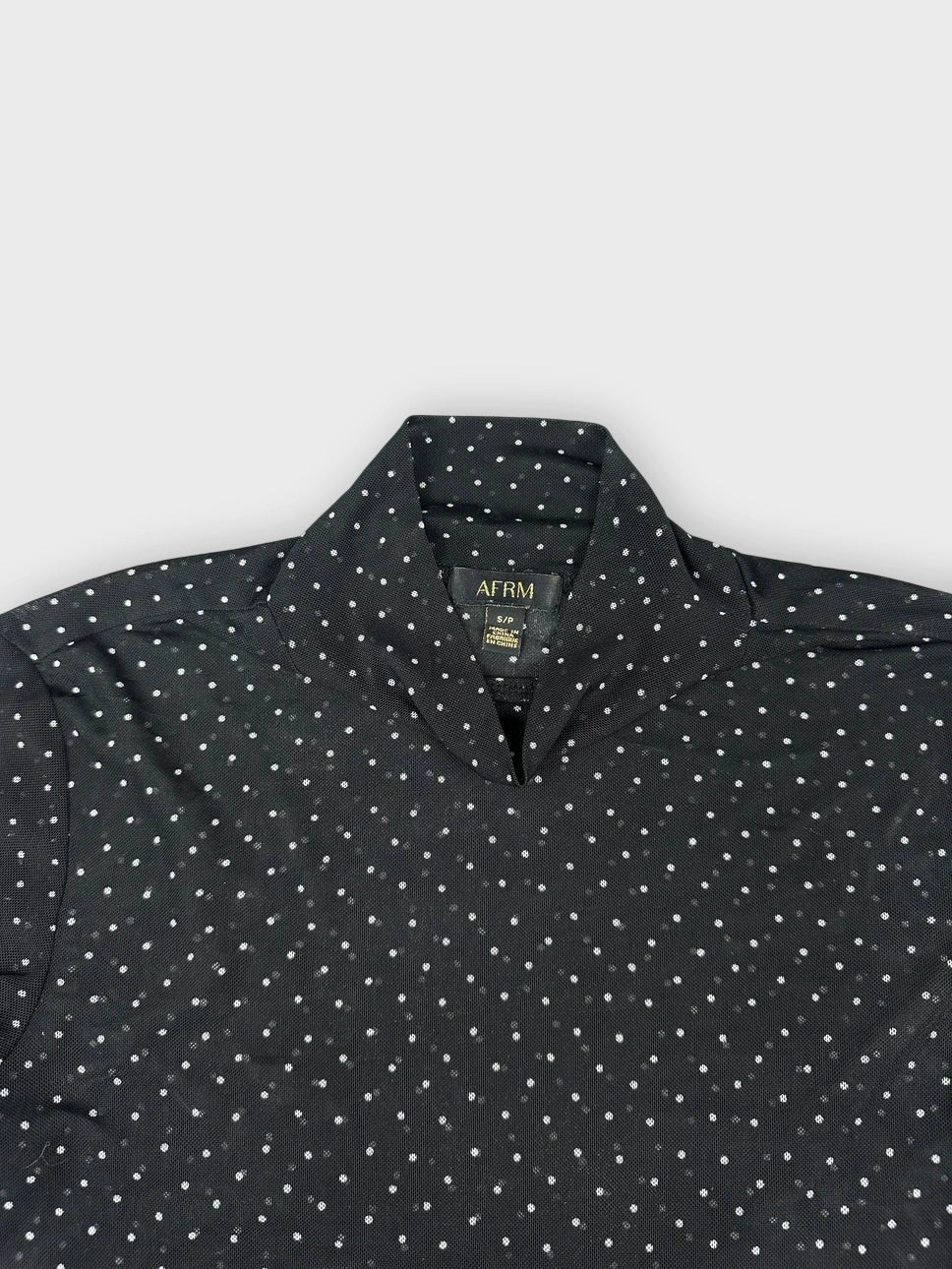 Detail view of sheer black long sleeve top with white polka dots.