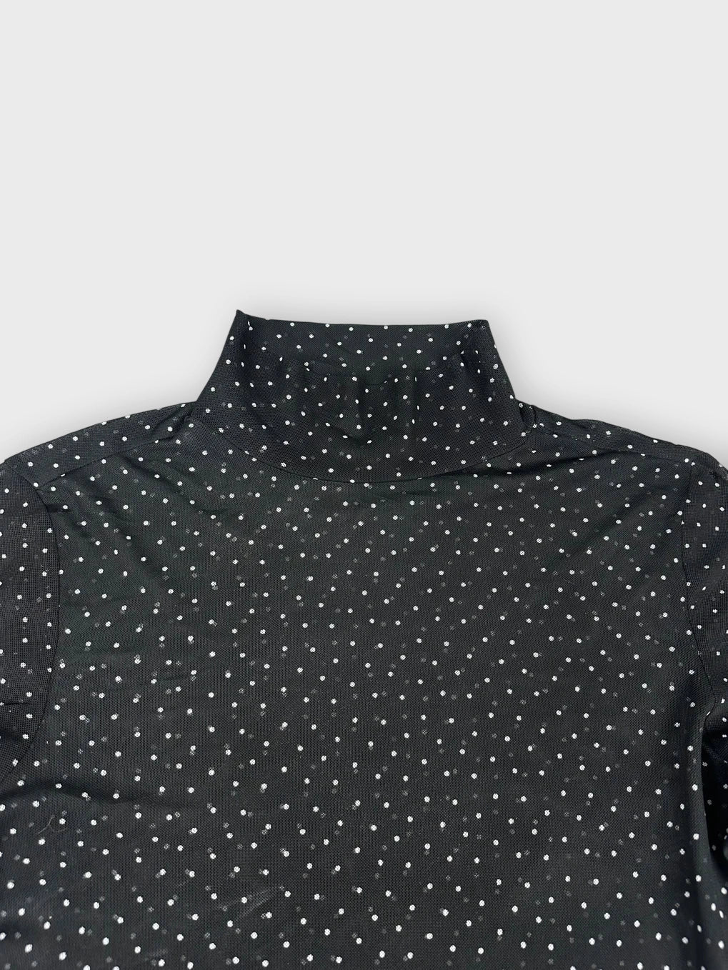 Detail view of a sheer black long sleeve top with polka dots.