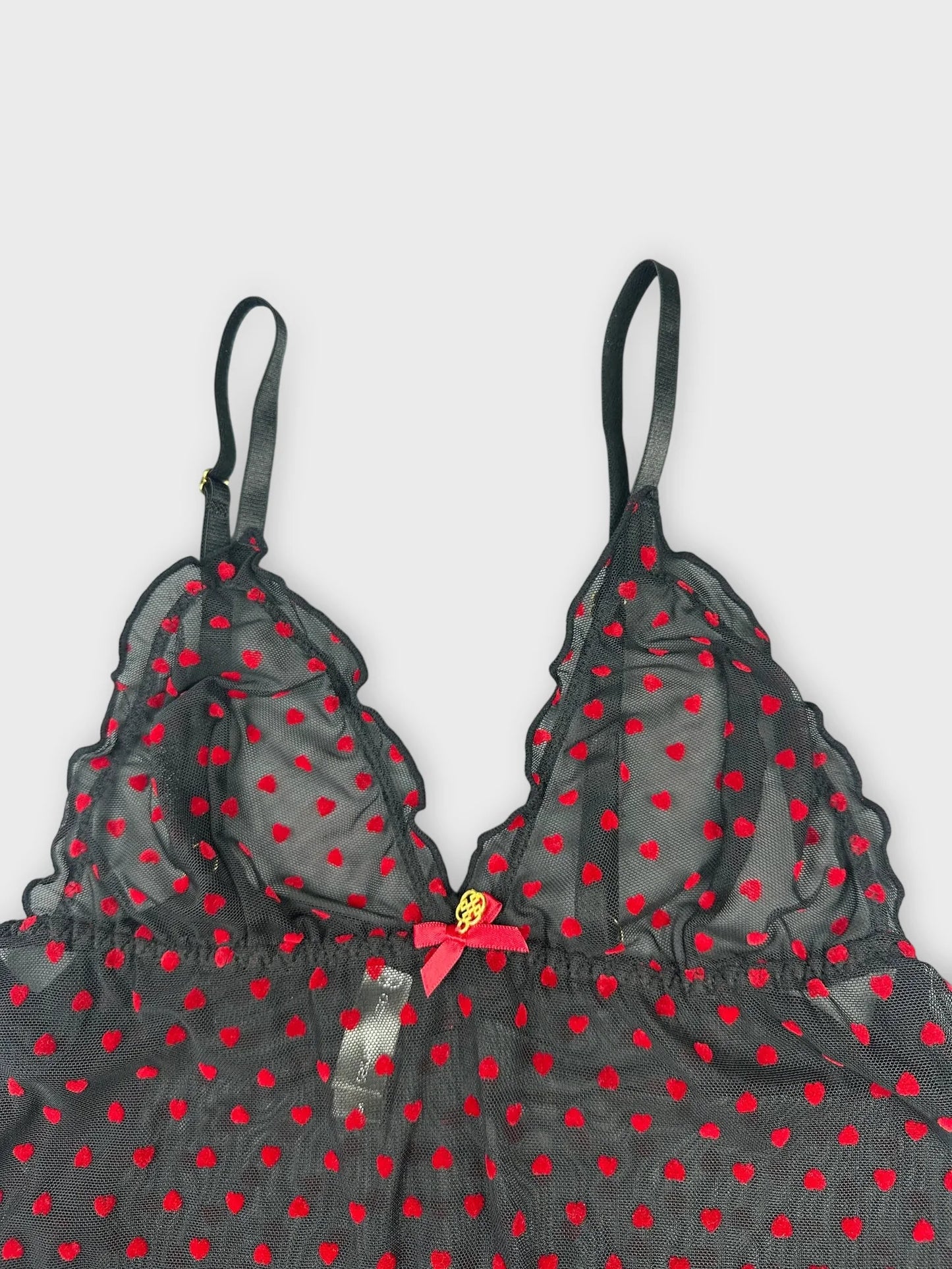 Detail view of a sheer black camisole with red polka dots and lace trim.