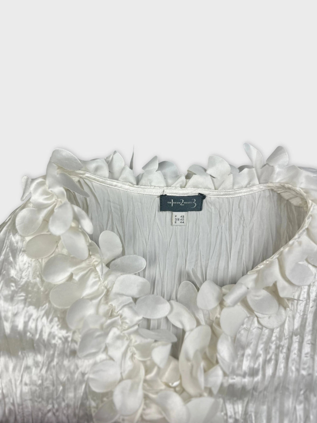 Detail view of a shiny white blouse with floral trim.
