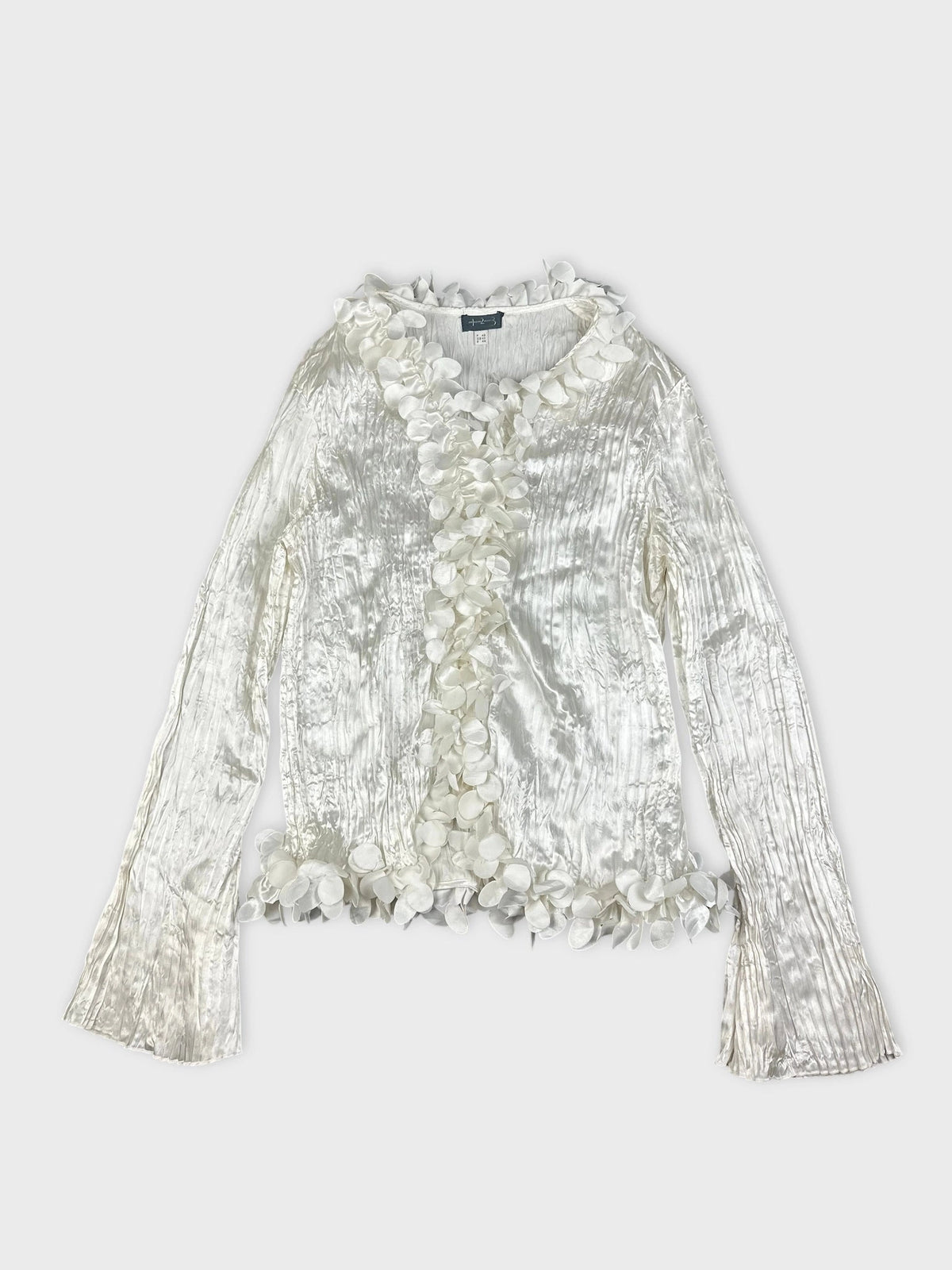 Detail view of shiny long sleeve white blouse with floral trim.