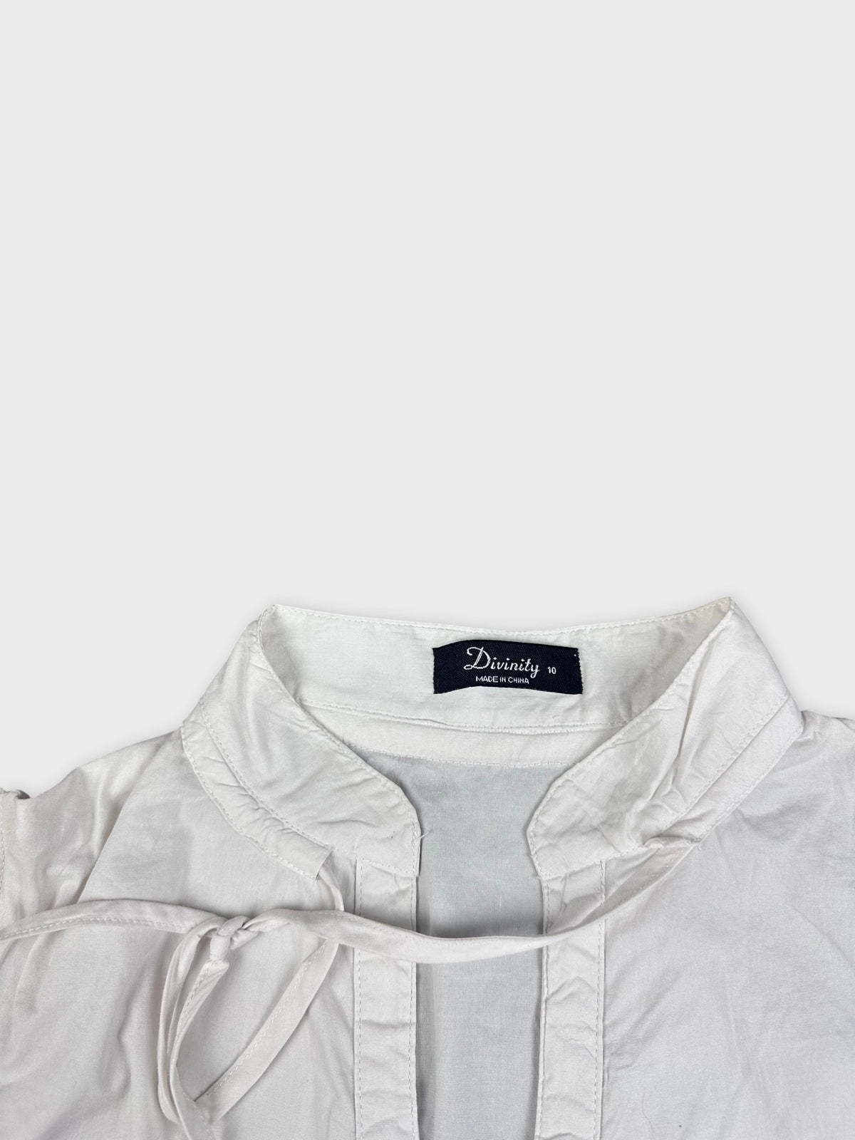 Detail view of short-sleeve white blouse featuring a tie neckline.