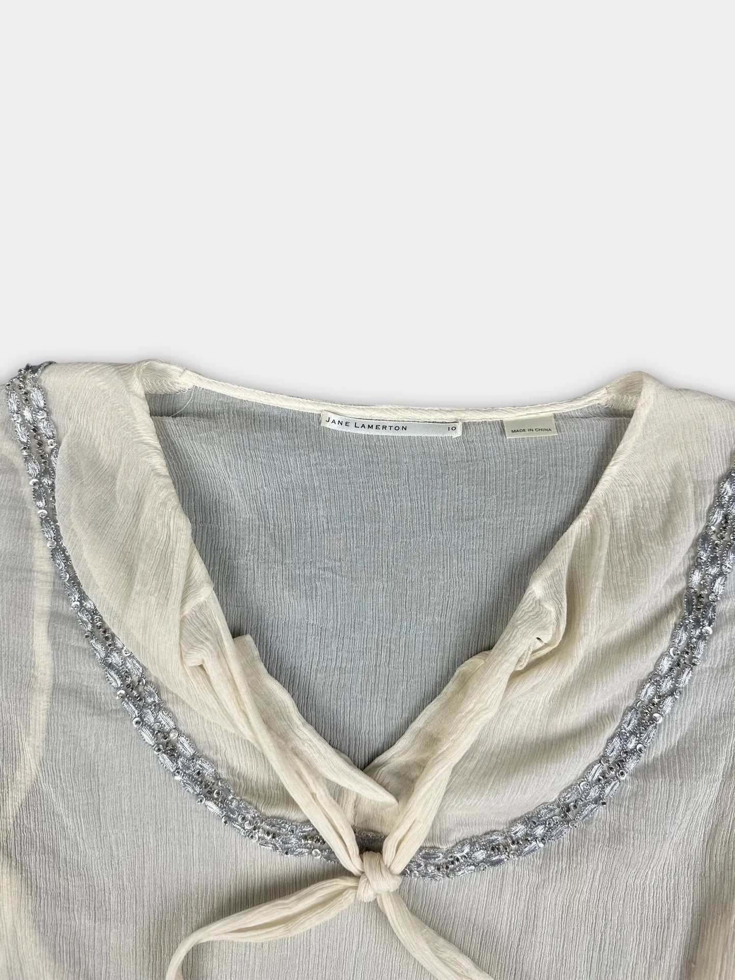 Detail view of a silk tie-front top in off-white with silver trim.