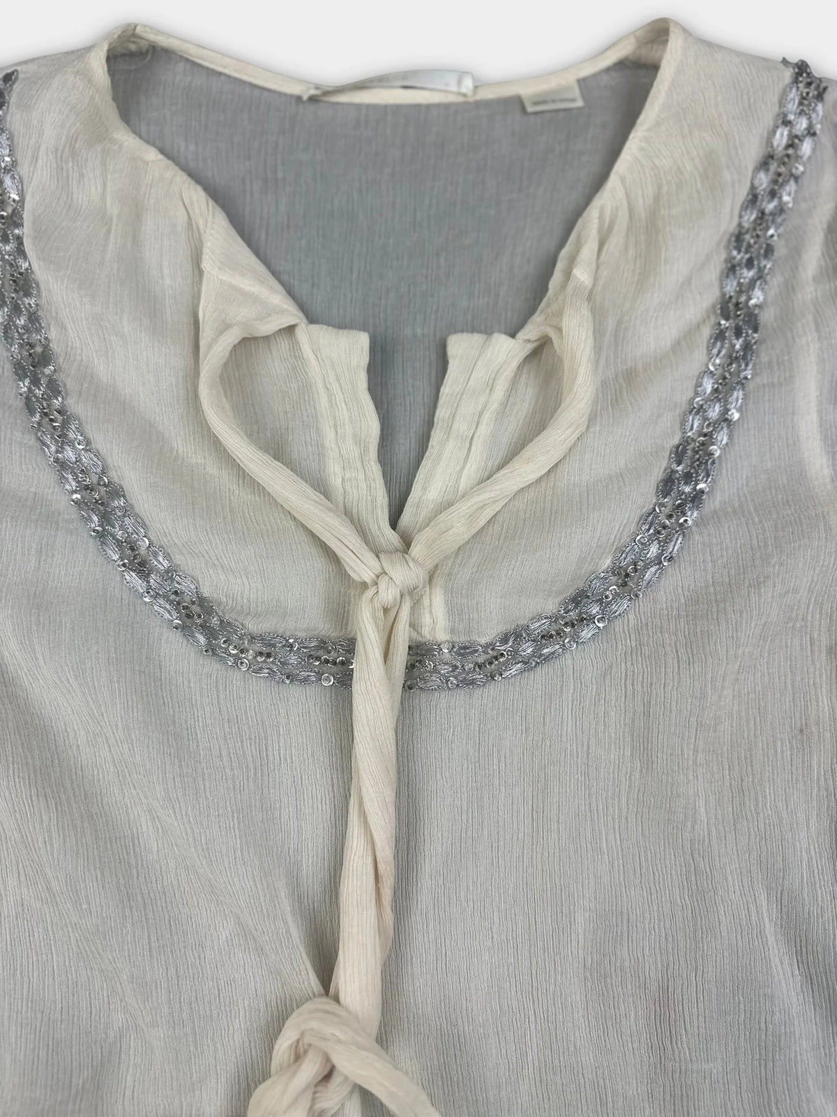 Detail view of silk tie-front top in cream with silver beaded trim.