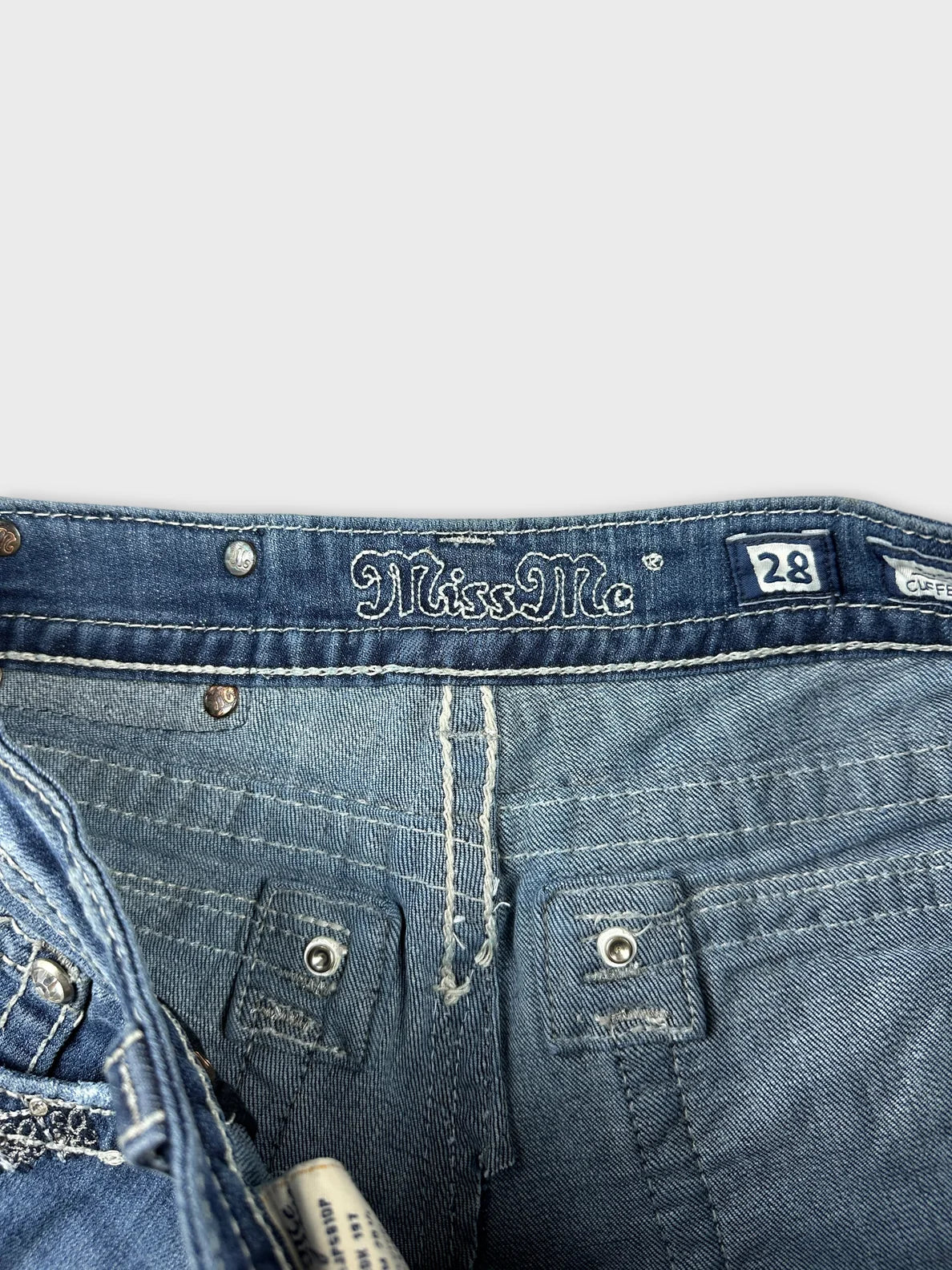 Detail view of a blue denim skirt with embroidered label and button details.