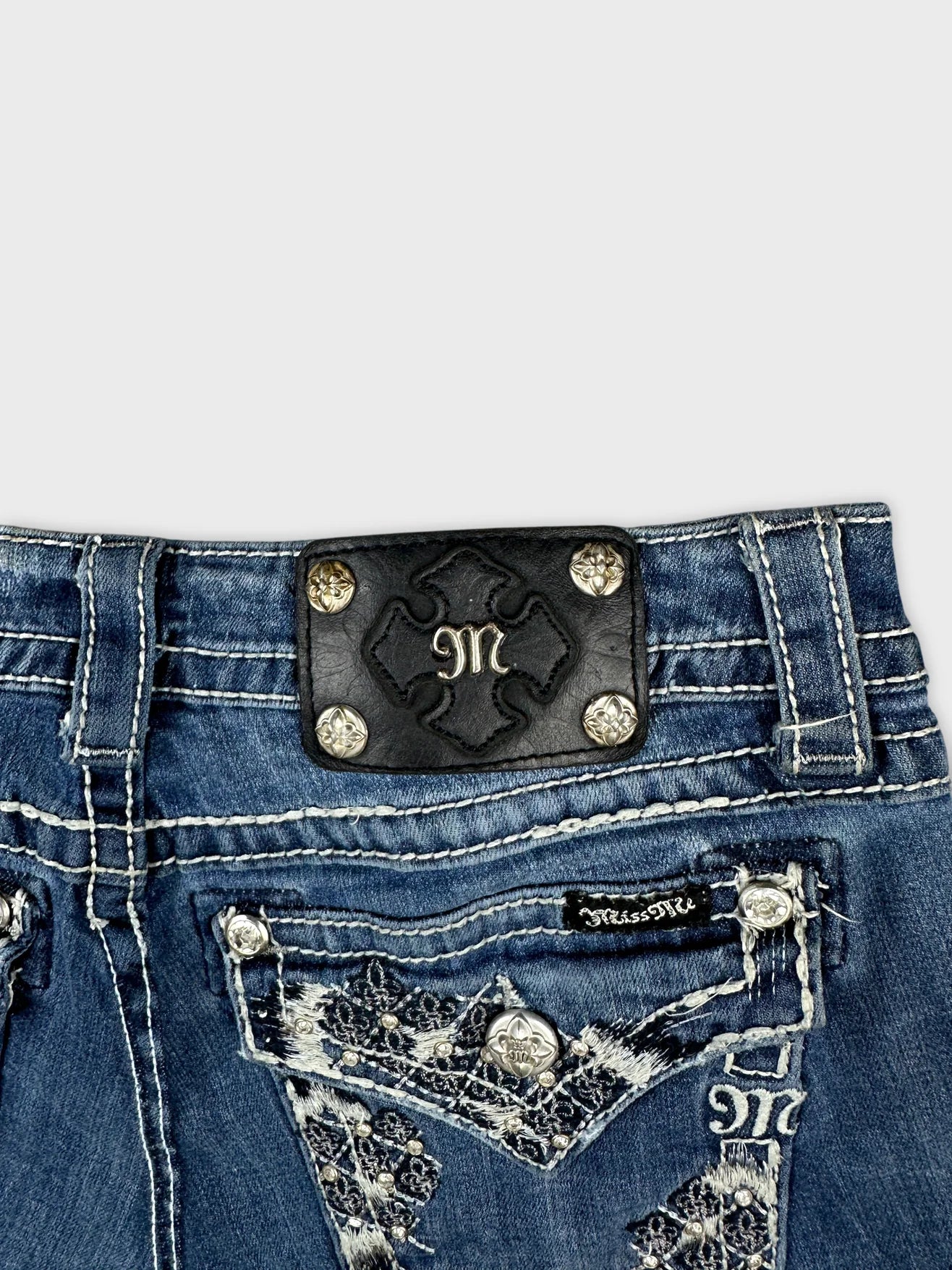 Detail view of blue denim skirt featuring embroidered pockets and decorative trim.