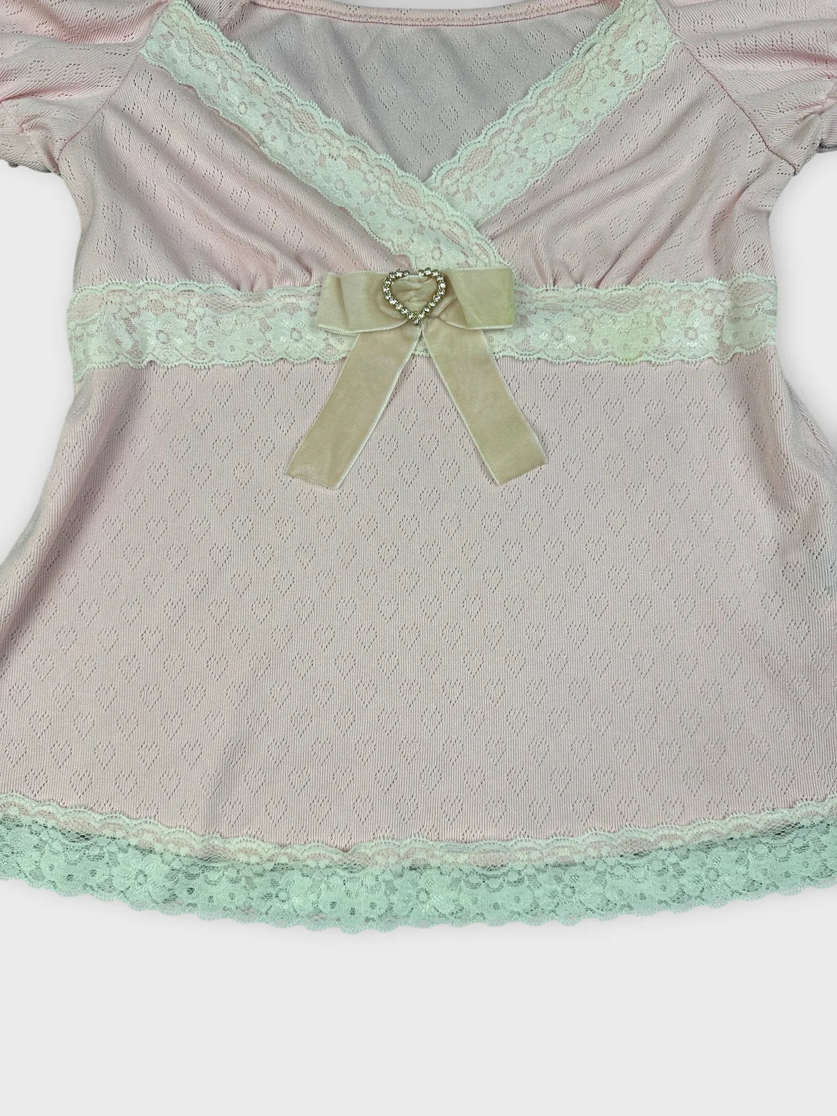 Detail view of soft pink blouse featuring lace trim and a bow.
