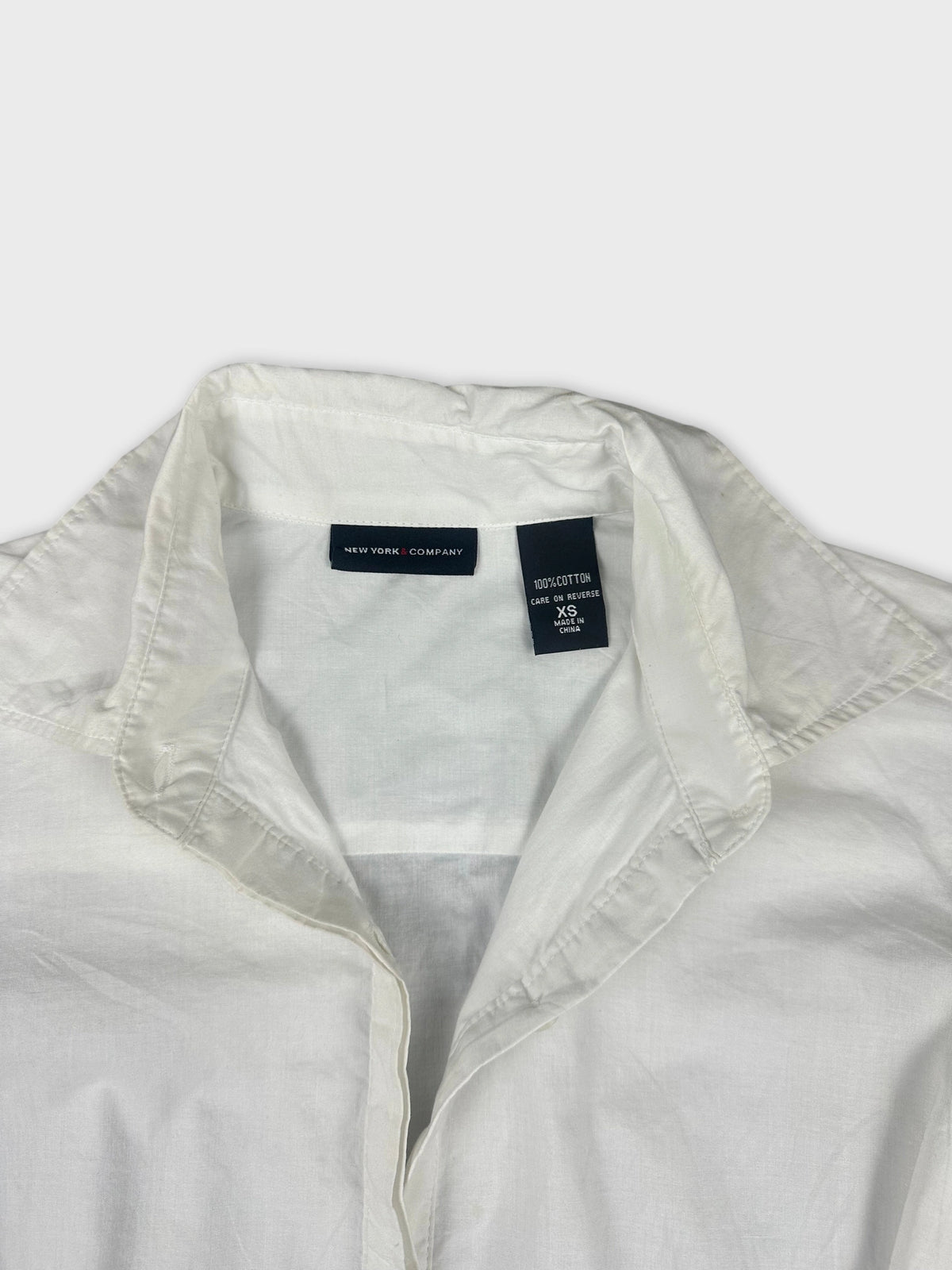 Detail view of a white cotton peplum button-up shirt collar and placket.