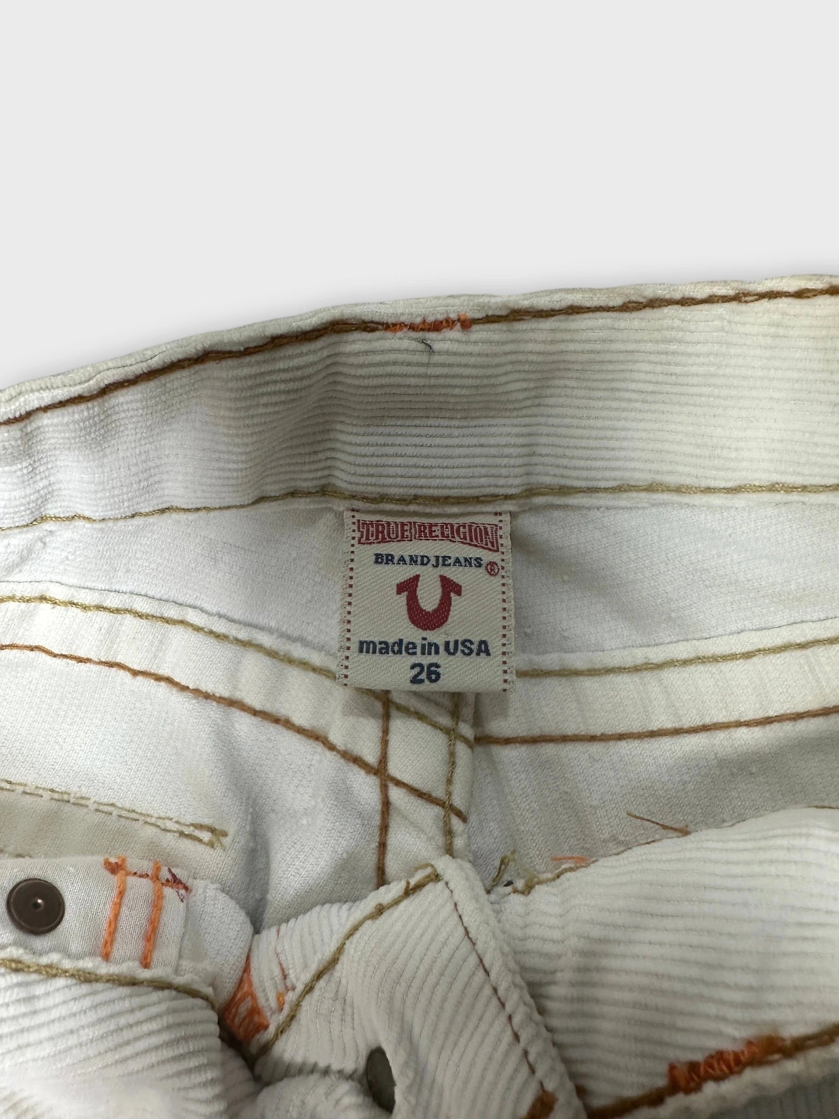 Detail view of white denim shorts with orange stitching and brand label.